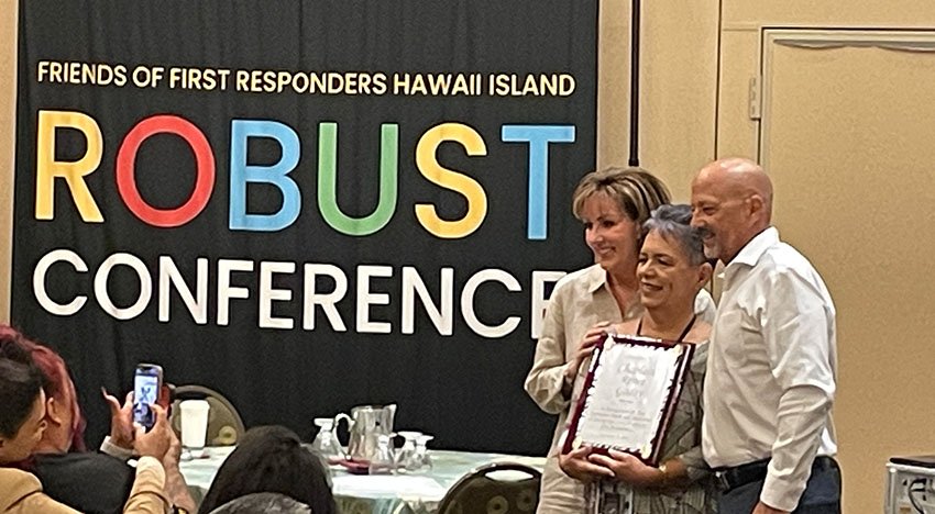 People posing for a photo at the Friends of First Responders Hawaii Island ROBUST Conference, with one person holding a certificate. Some attendees are seated and taking pictures.