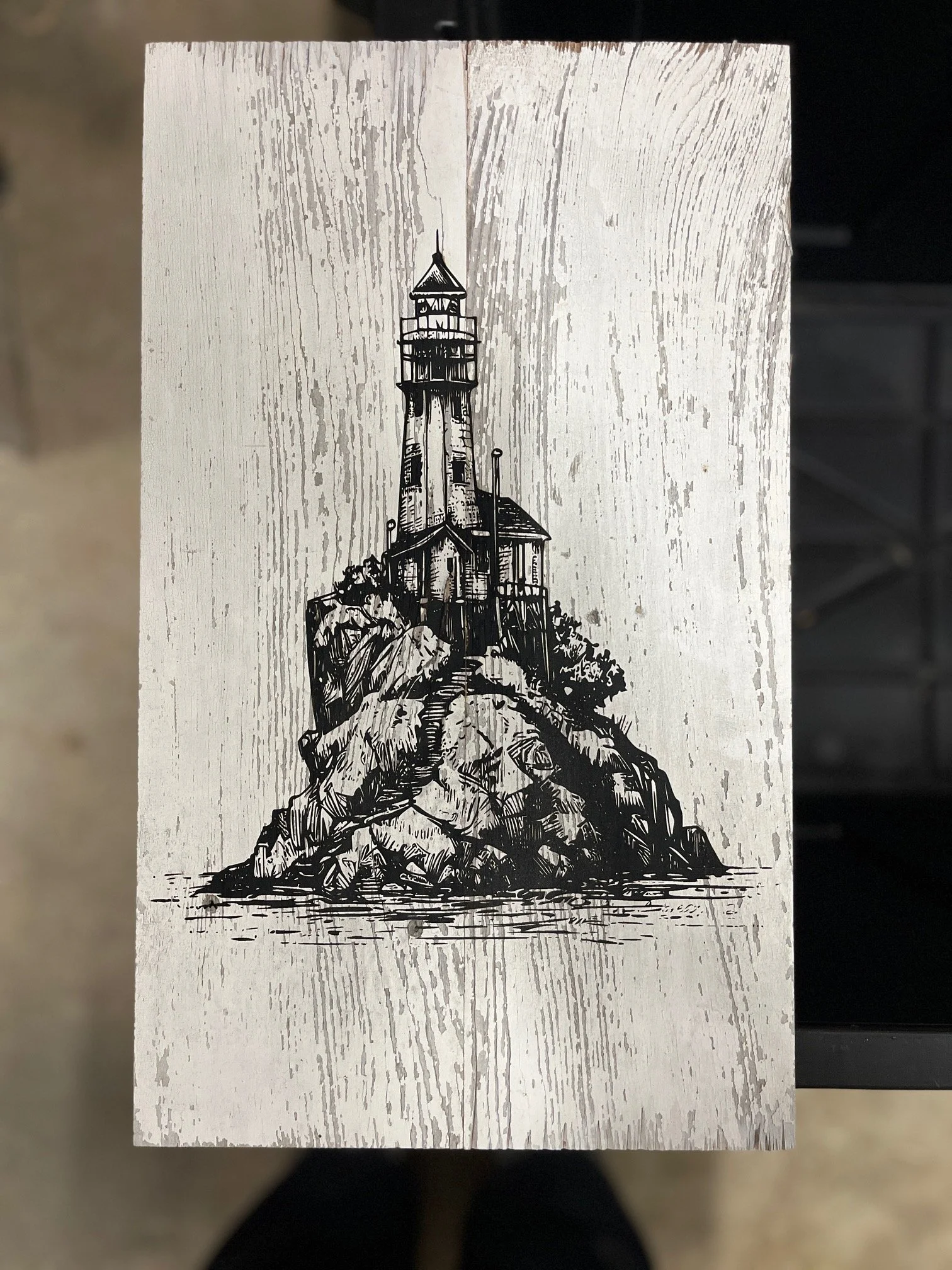 Black and white illustration of a lighthouse on a rocky island with trees, water in the foreground, and a wooden background.