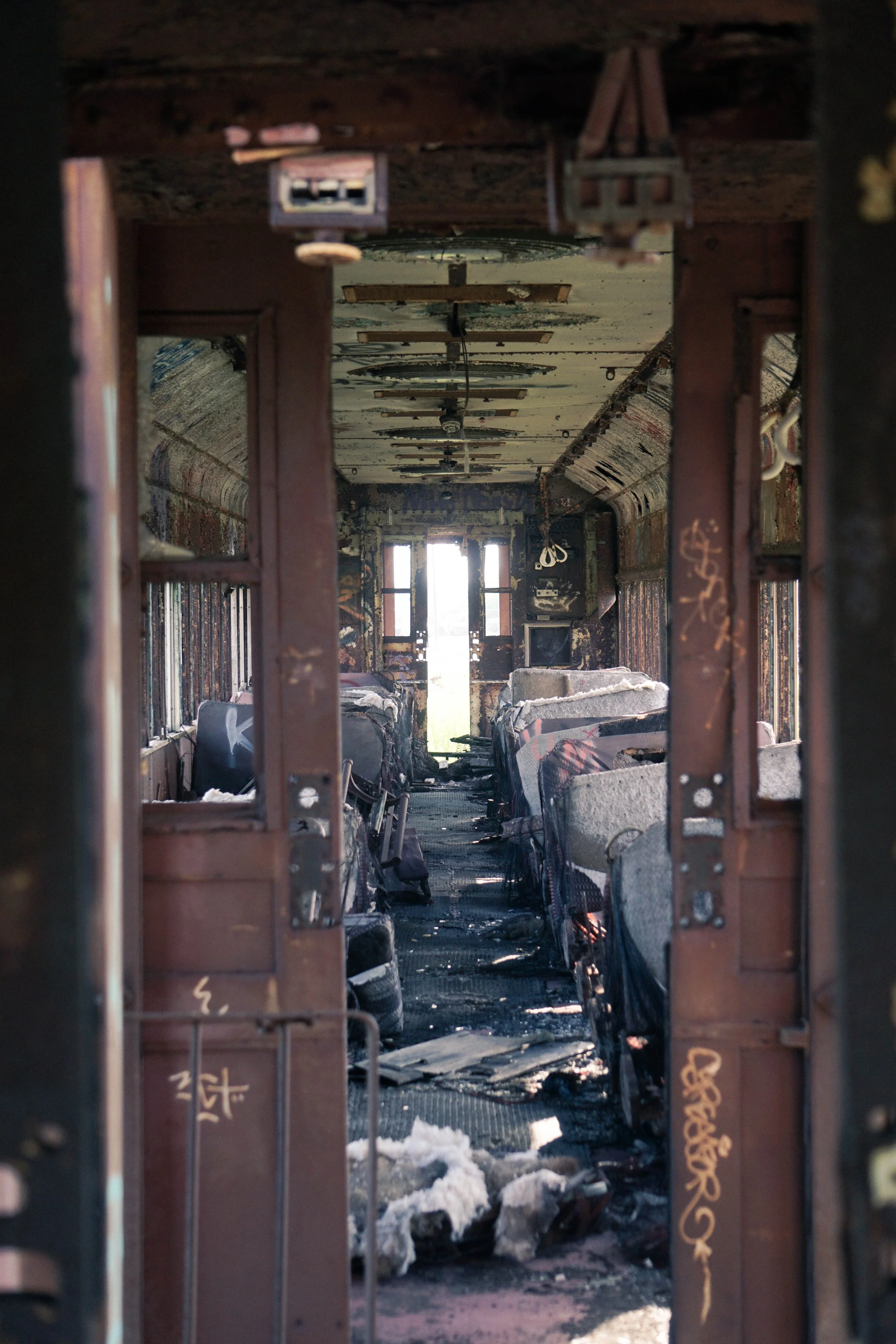 Inside a burned-out school bus, showing damaged seats, darkened walls, and lighting from the open door at the rear.
