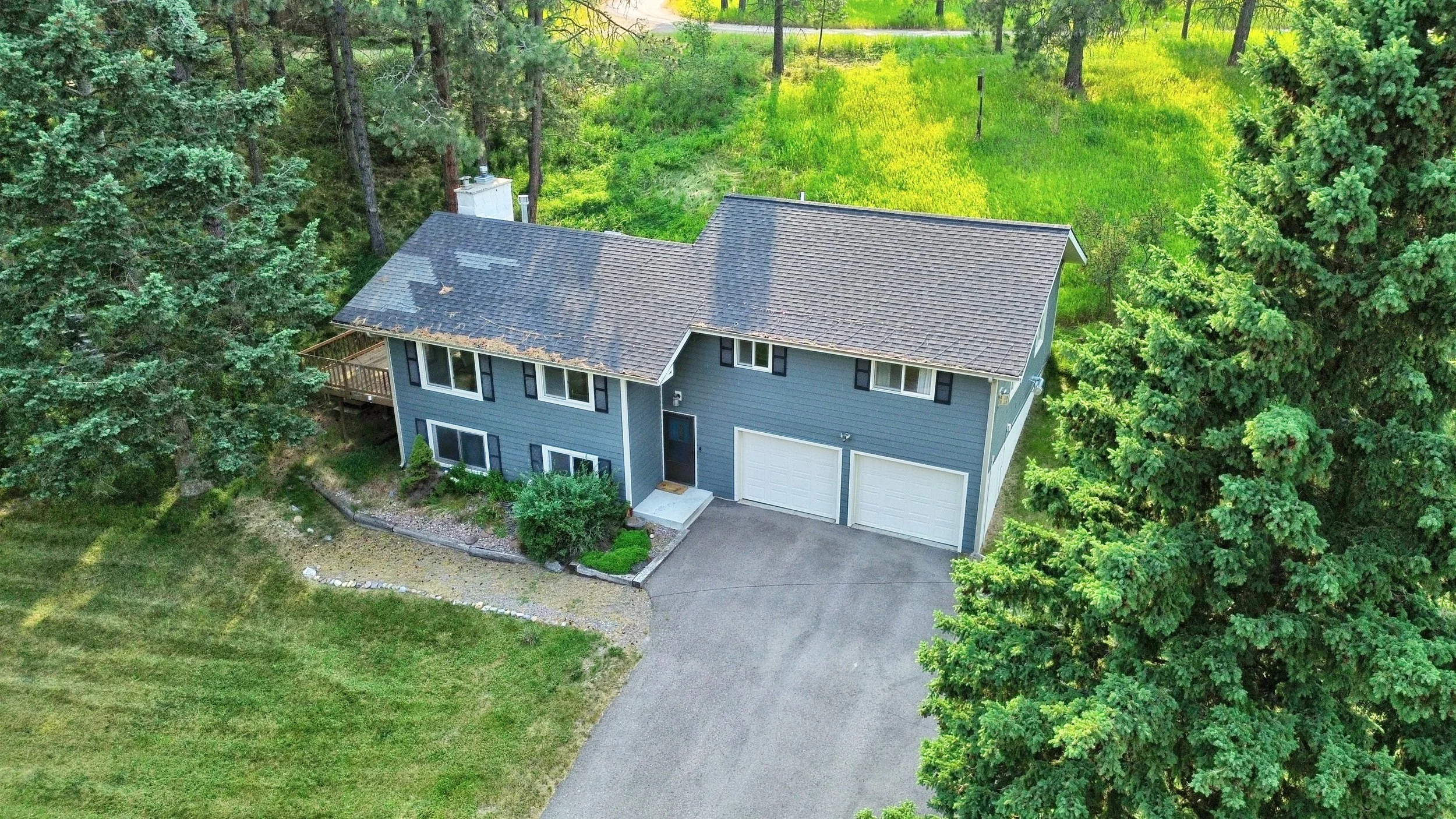 Aerial view of a blue two-story house with a white garage door, surrounded by tall green trees and a grassy backyard.