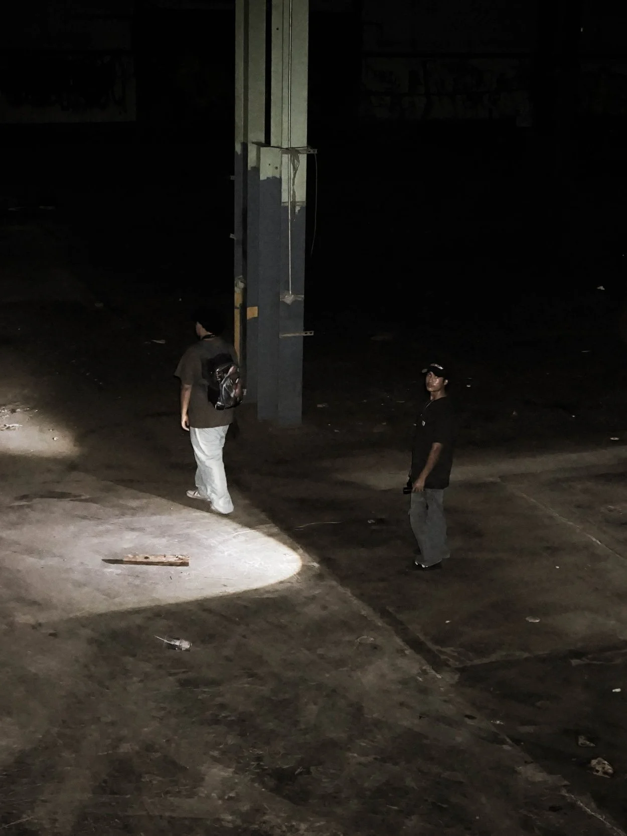 Two people standing in a dark, empty parking lot illuminated by a single bright light.