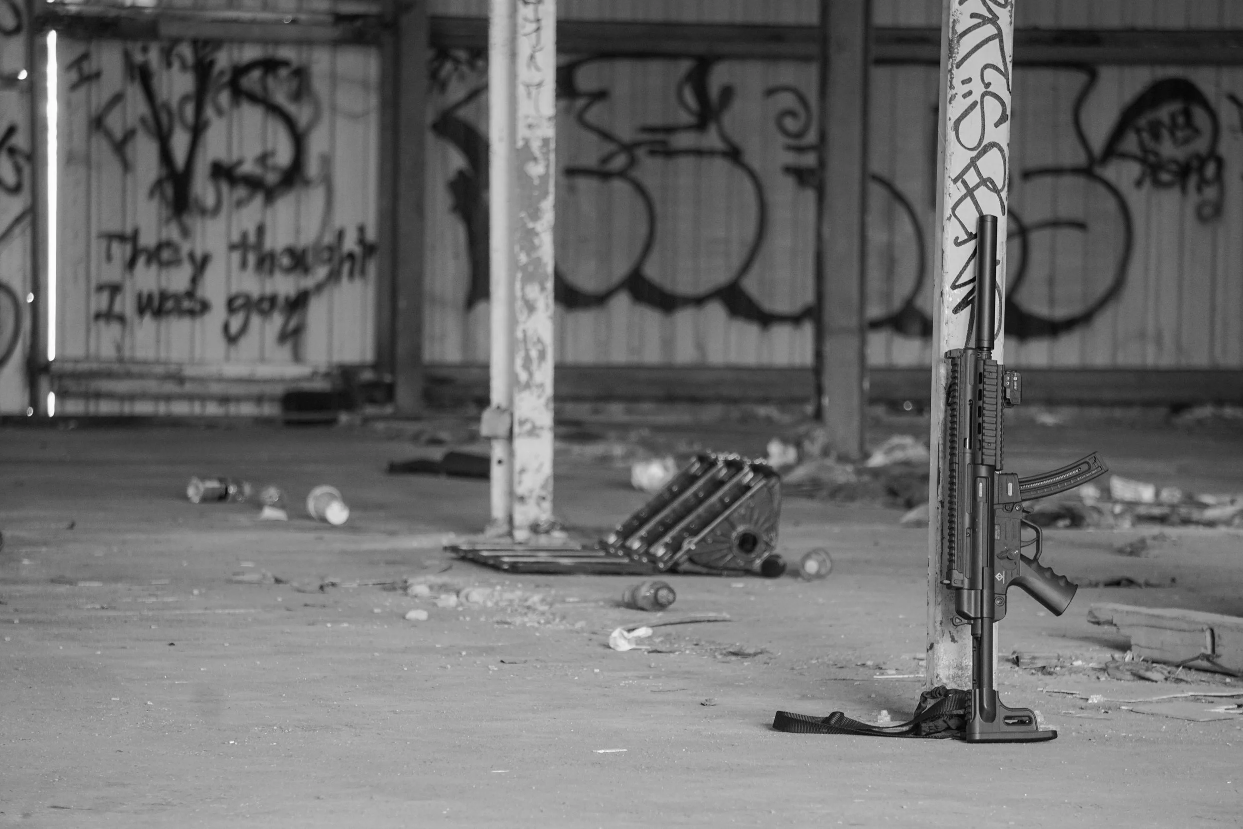 A semi-automatic rifle leaning against a support in an abandoned area with graffiti on the walls and trash on the ground.