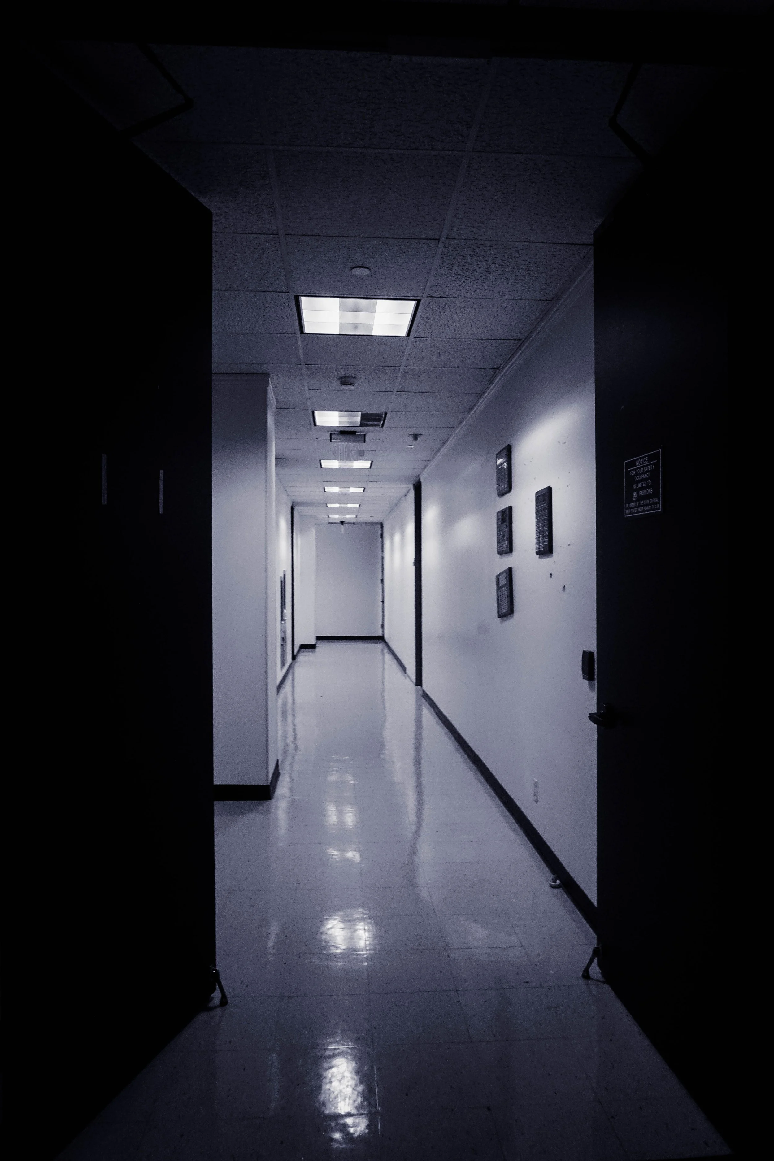Empty hospital or office corridor with white walls, shiny tiled floor, and ceiling lights.