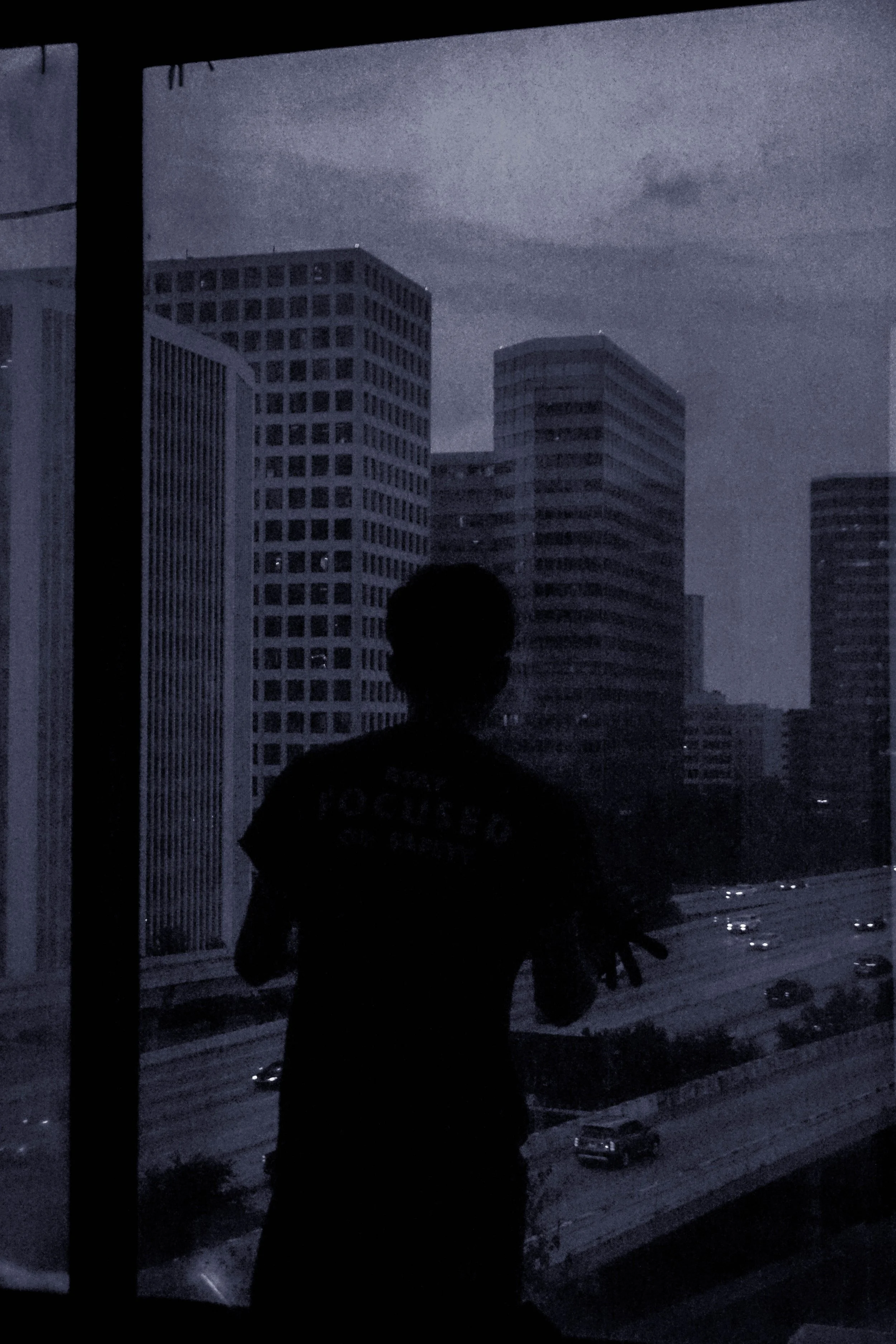 Silhouette of a person taking a photo inside a building, with a cityscape of tall buildings and a highway visible through a window