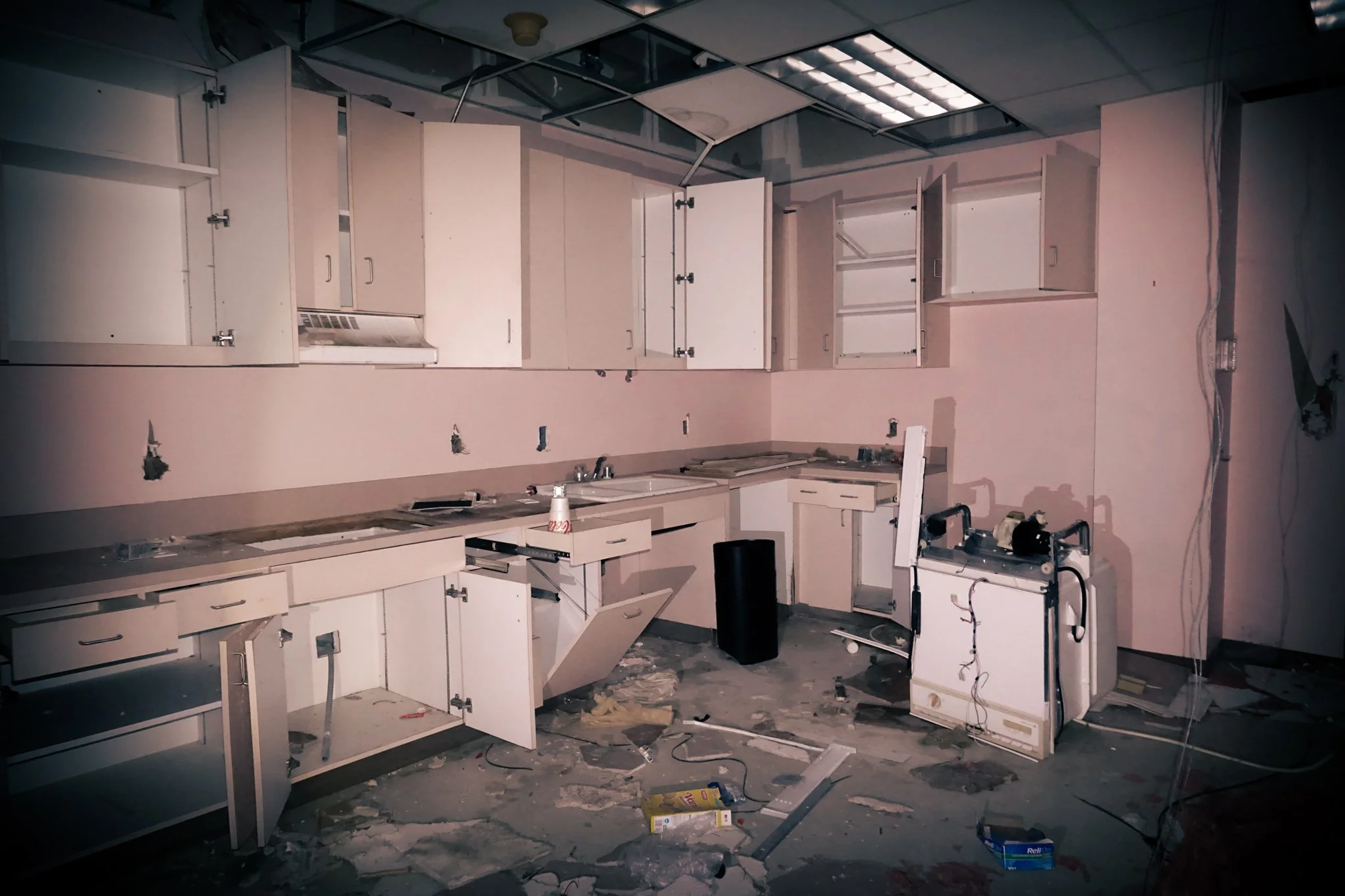 Damaged kitchen with open cabinets, debris on the floor, and missing appliances.
