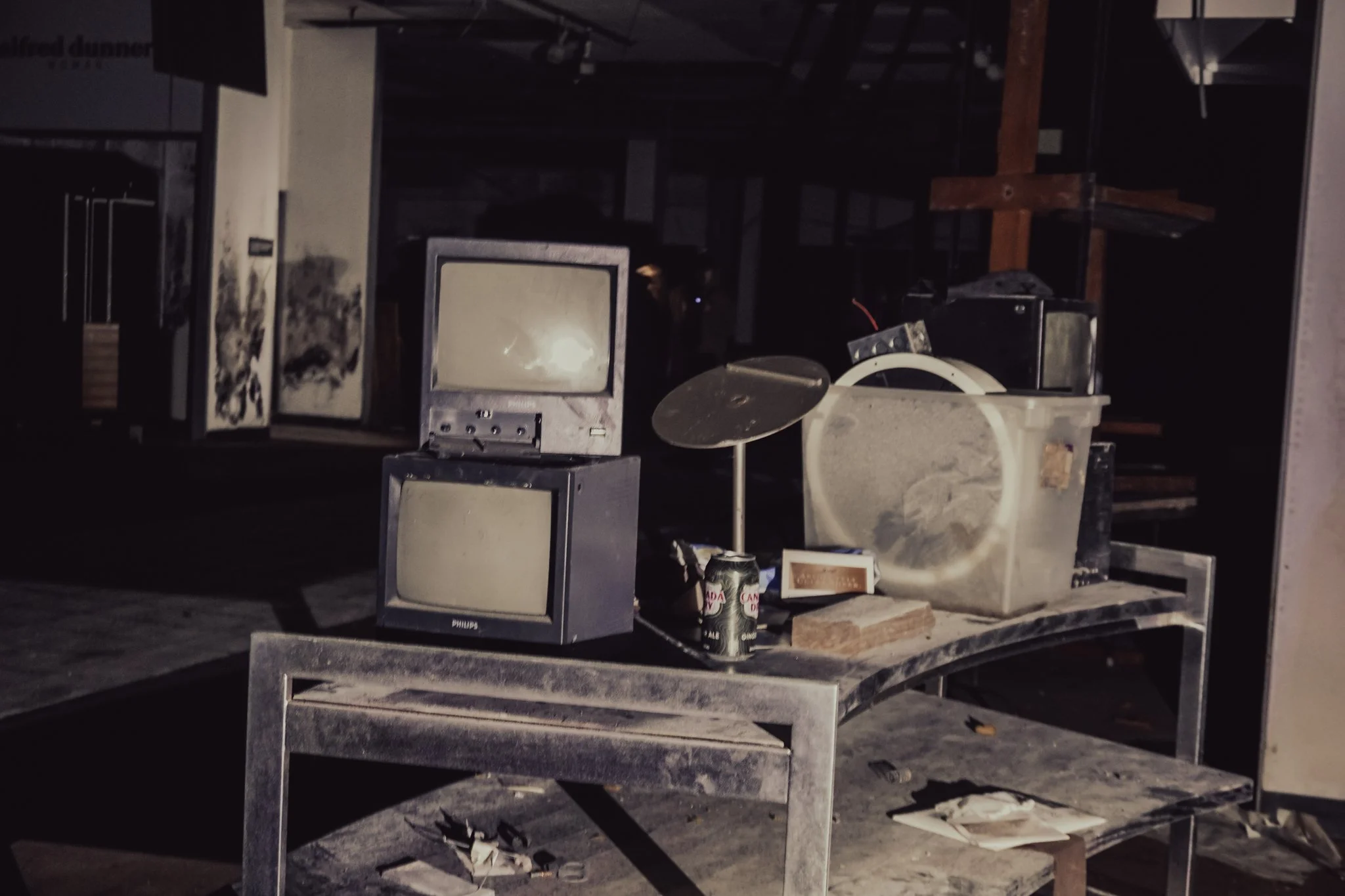 Dust-covered old electronics and objects on a metal table in a dark, abandoned space.
