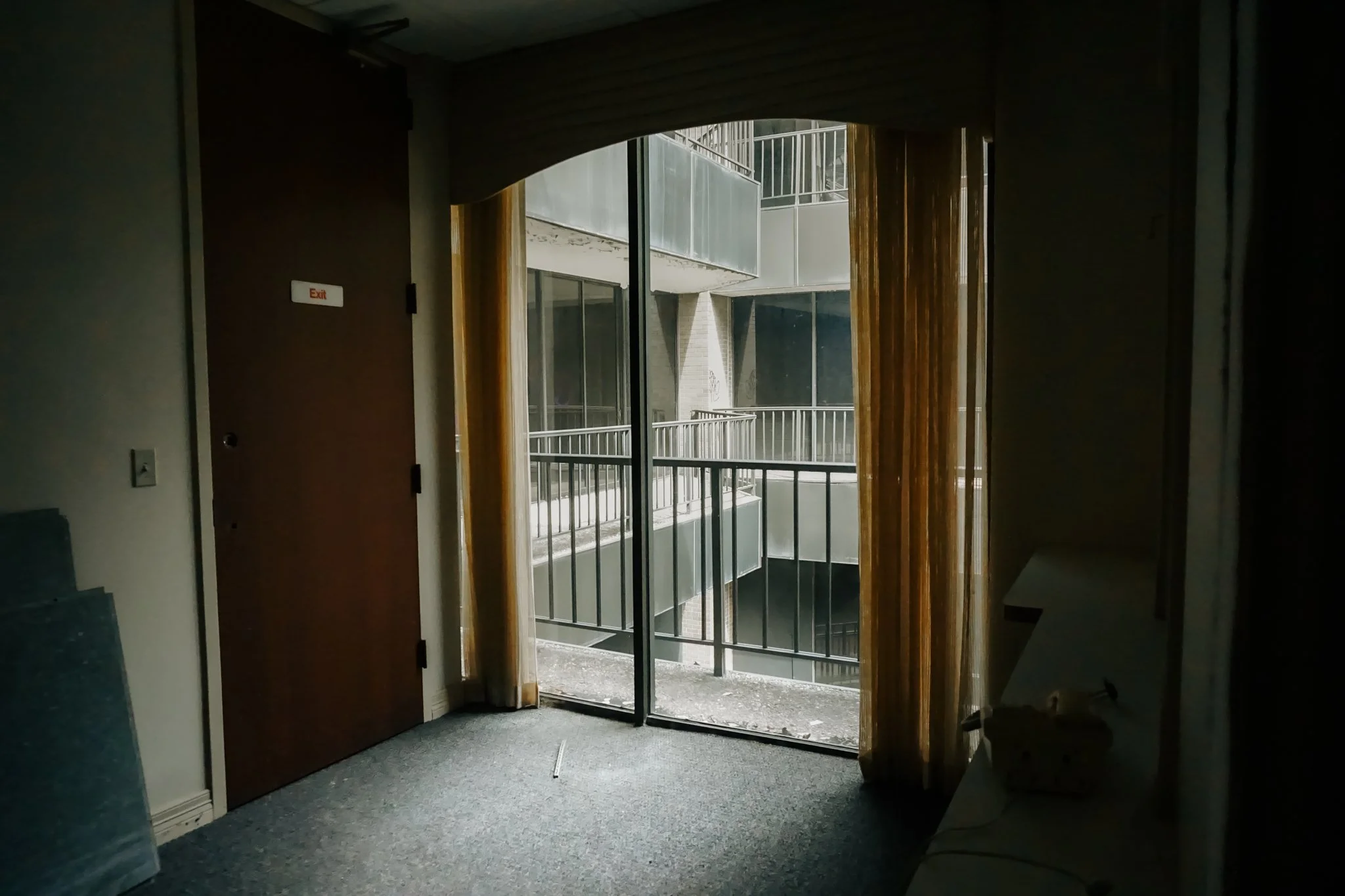 Dark interior room with sliding glass door, yellow curtains, and view of a concrete balcony and neighboring building with balconies.