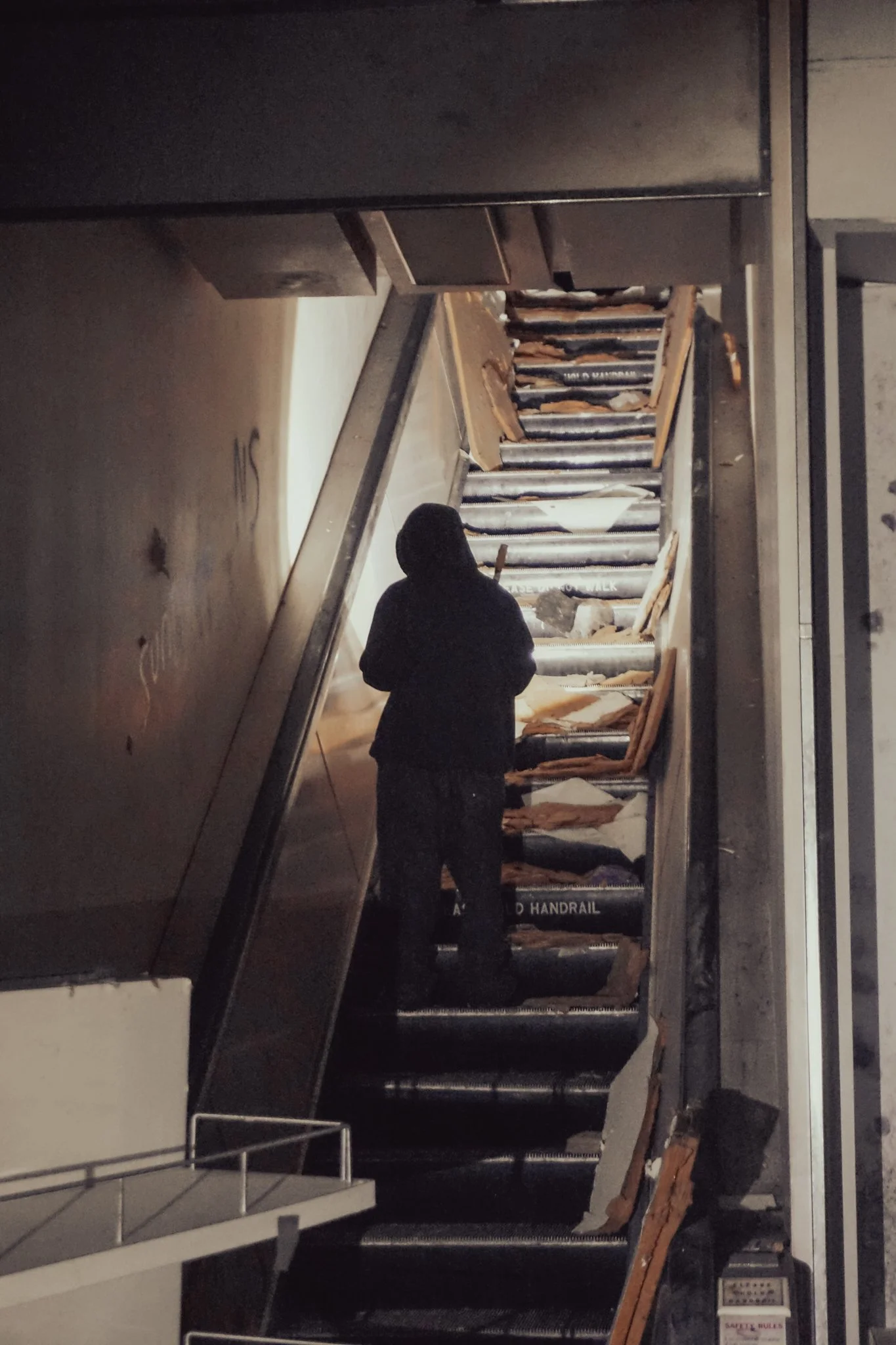 Person standing on an escalator with damaged steps and debris, in a dimly lit environment.