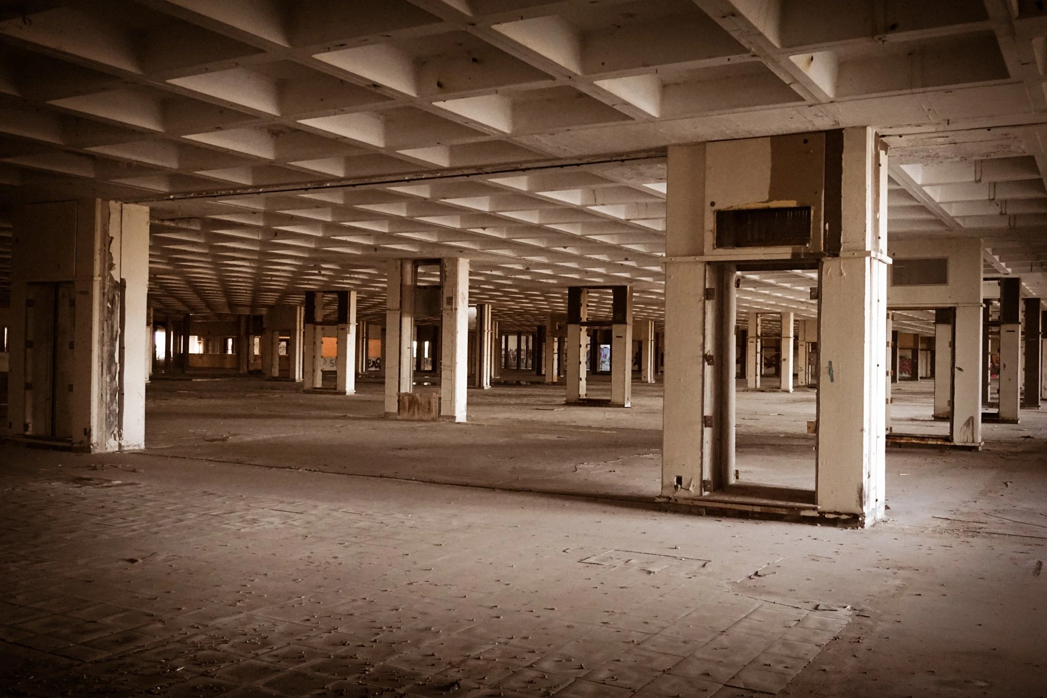 An empty, abandoned retail store with exposed ceiling beams, concrete pillars, and worn flooring.
