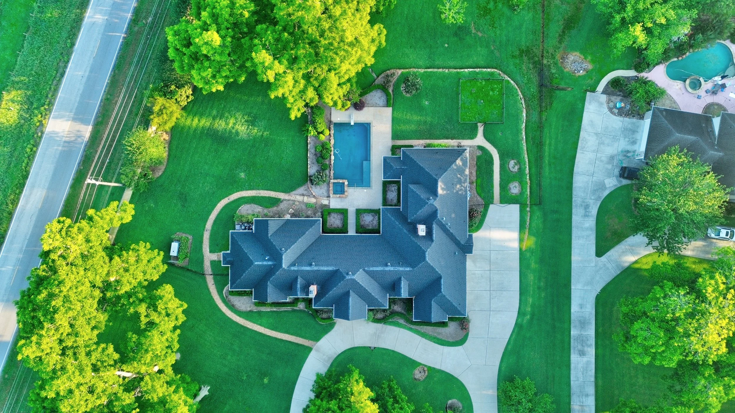 Aerial view of a house with a backyard, swimming pool, green lawn, and trees.