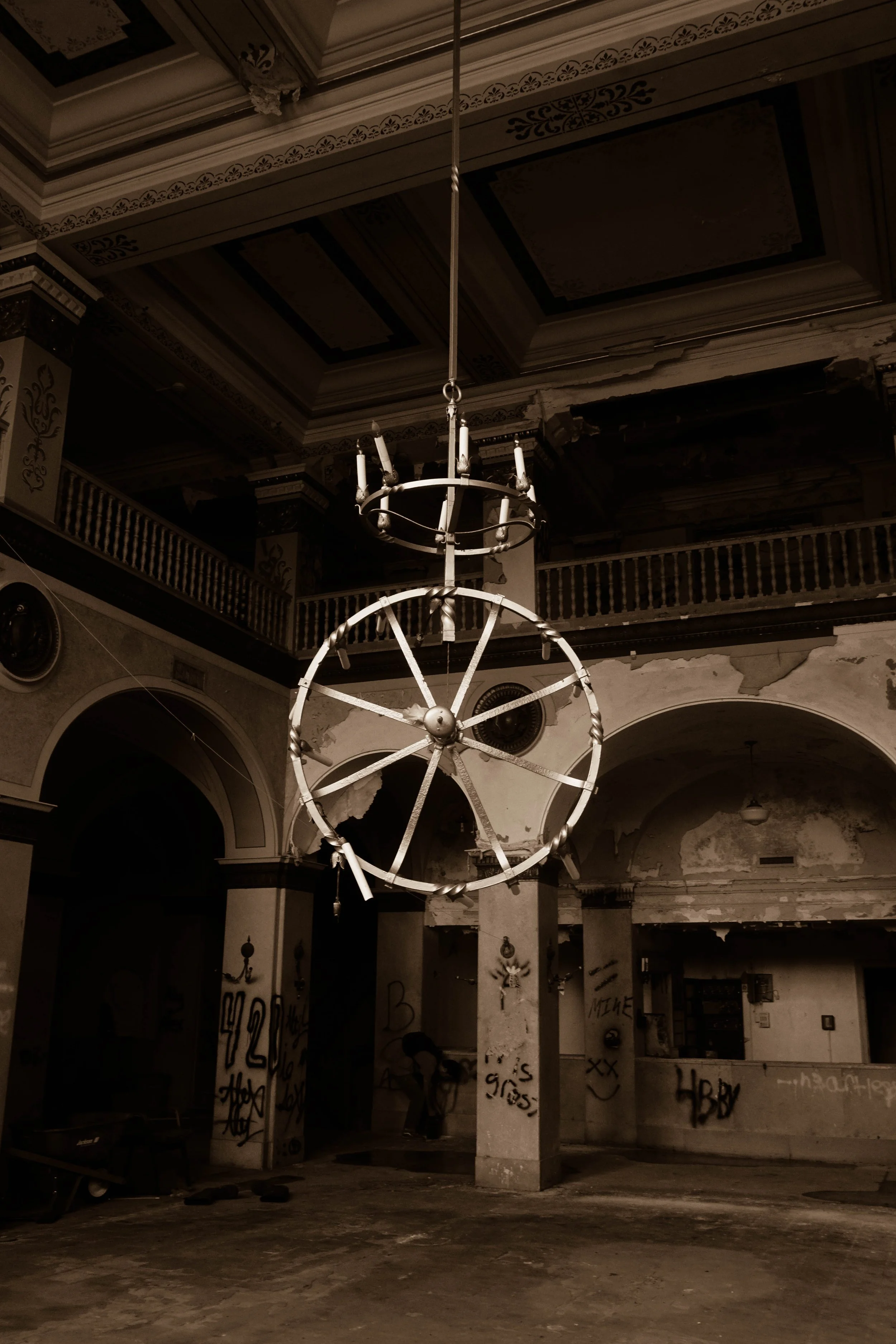 An abandoned building with peeling paint, graffiti on walls, and a large, broken circular chandelier hanging from the ceiling.