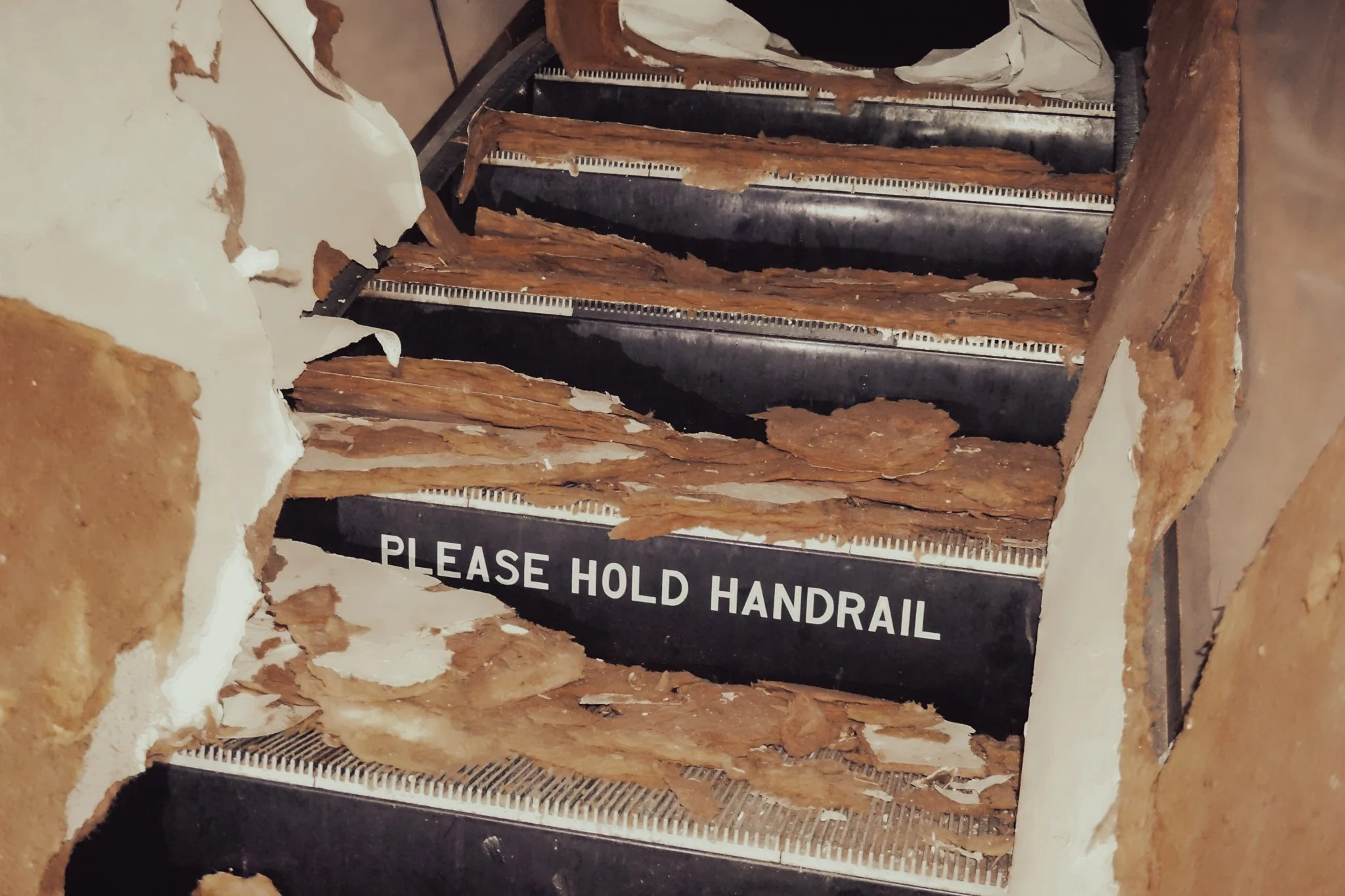 Broken staircase with wood and plaster debris, and a sign that reads 'Please Hold Handrail'.