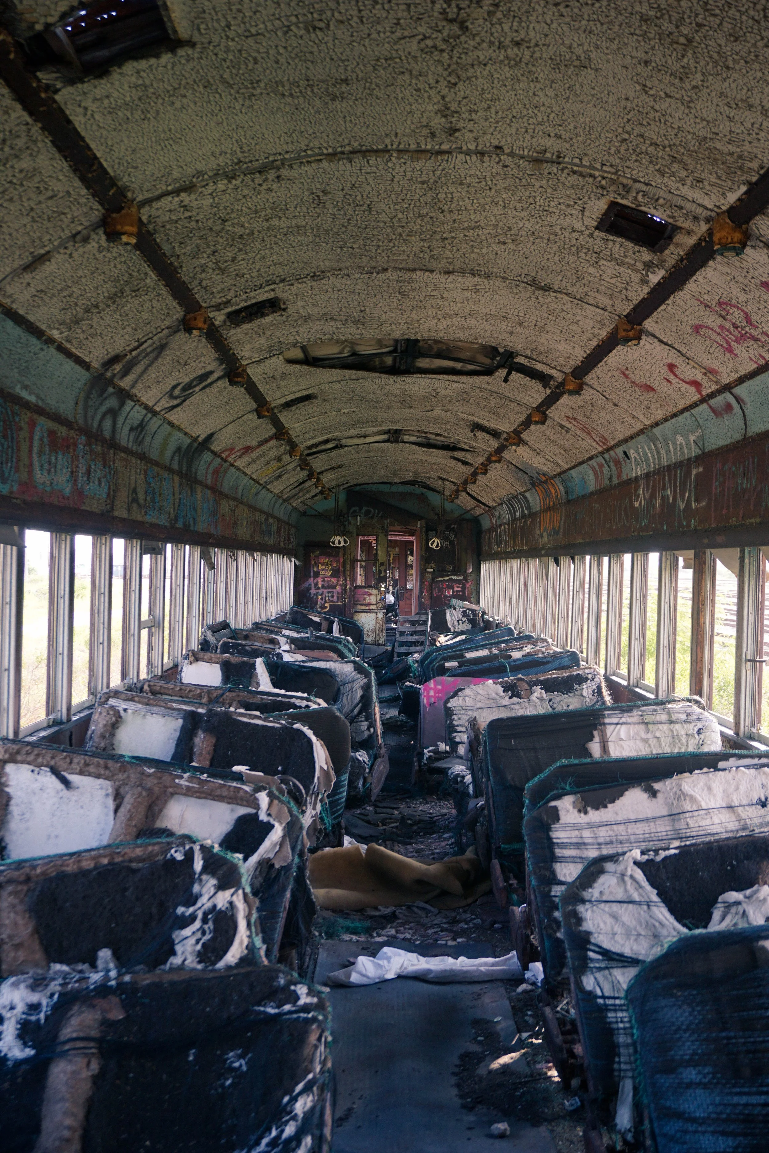 The interior of a burned-out, abandoned train car with charred seats and walls covered in graffiti.