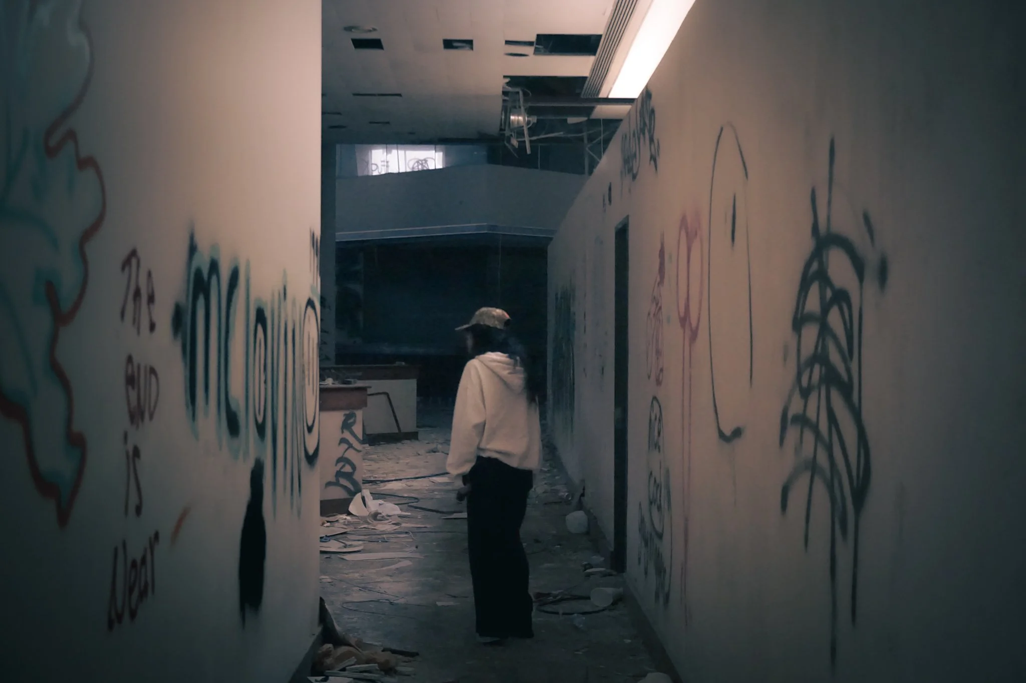 Person standing in a partially abandoned and vandalized office with graffiti on the walls.