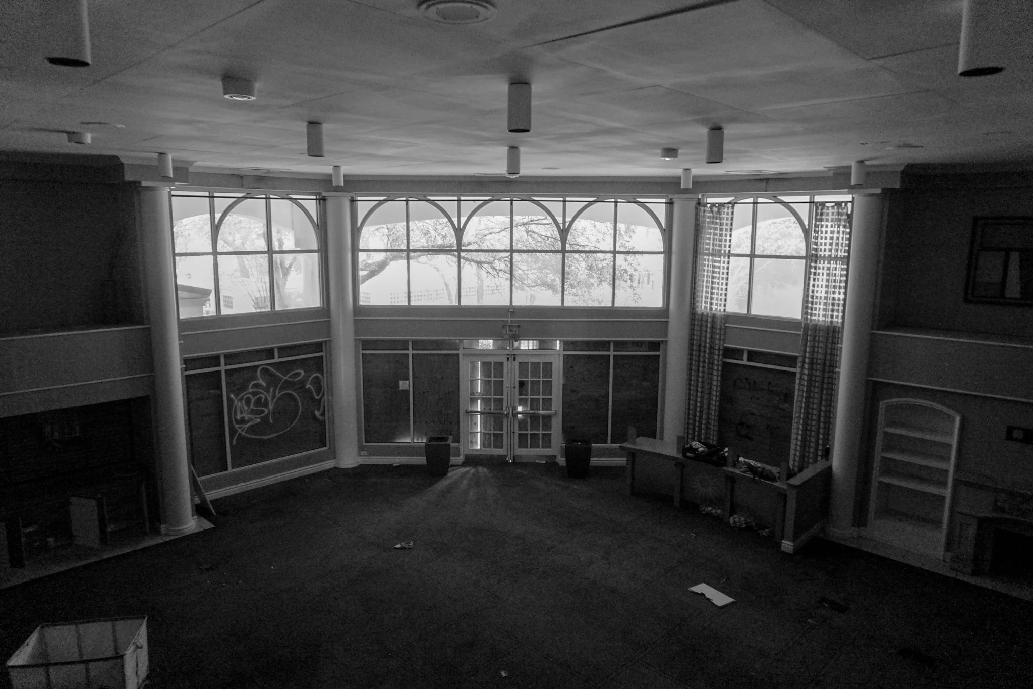Empty room with large windows, some curtains, and a door, possibly a lobby or a common area, in black and white.