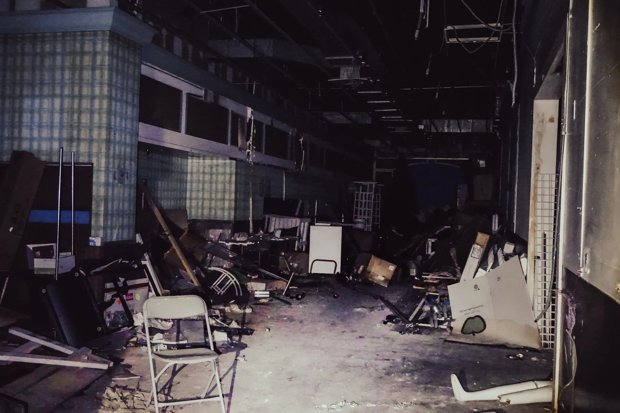 Cluttered and damaged store interior with debris, broken furniture, and exposed ceiling wires.