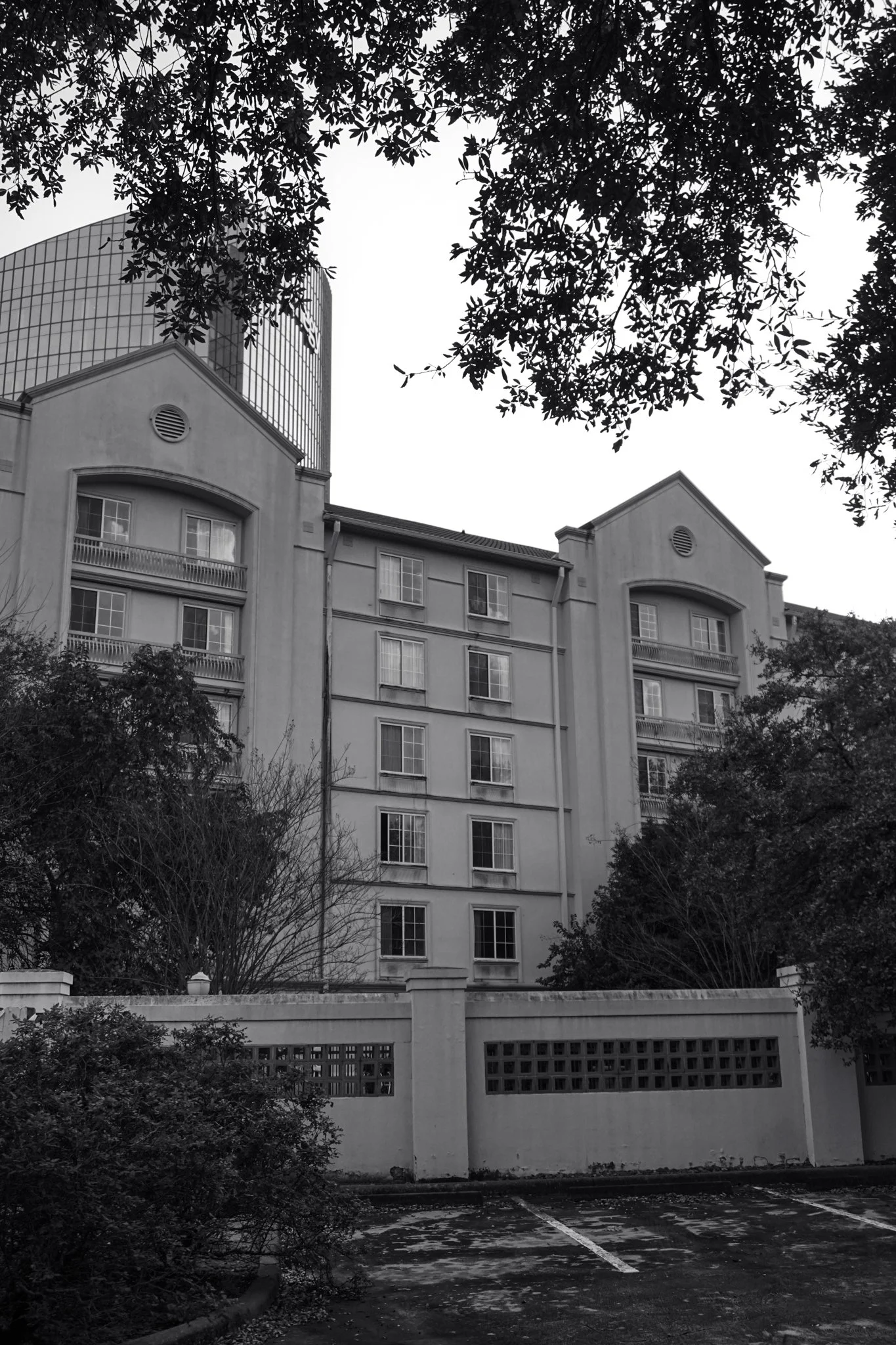 Black and white photo of a multi-story residential building with trees and a parking lot in the foreground.