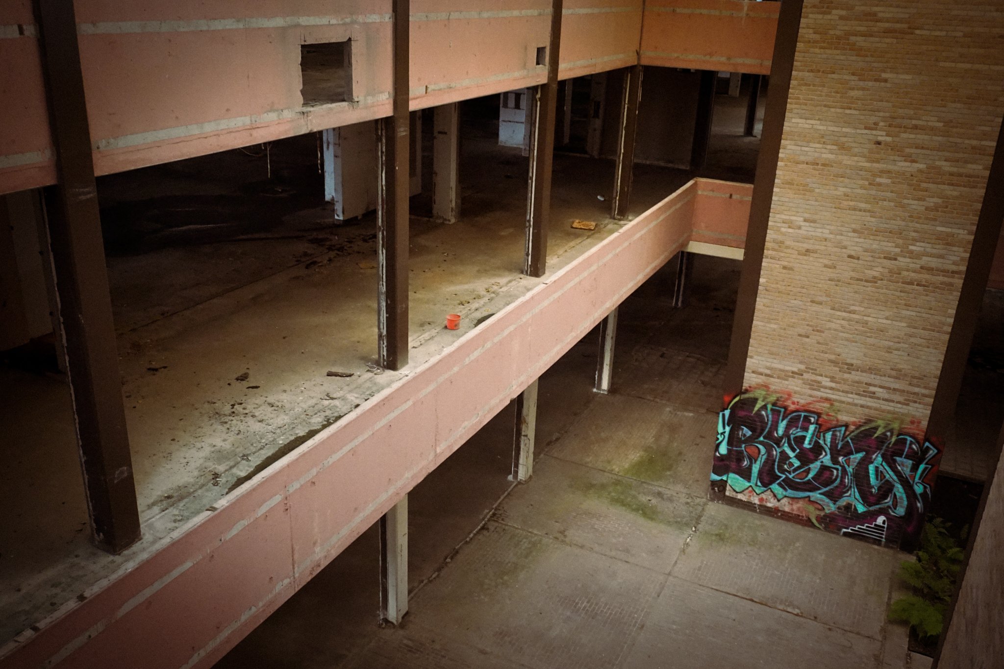 Empty, abandoned building interior with graffiti on wall, showing multiple floors and exposed structural elements.