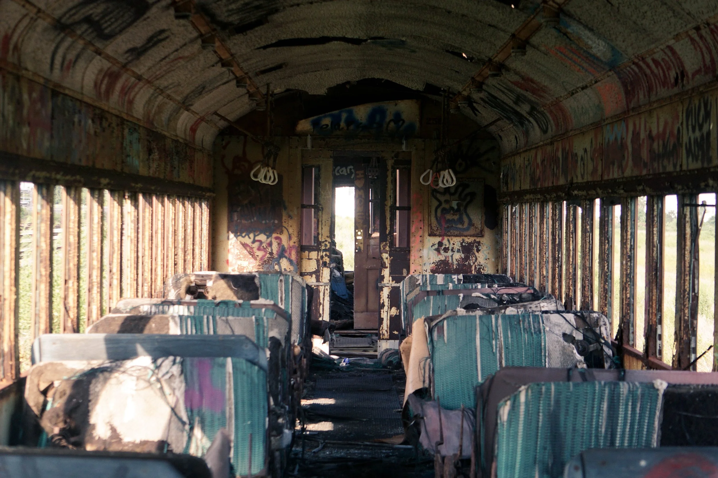 Inside an abandoned, graffiti-covered bus with burnt seats and damaged interior.