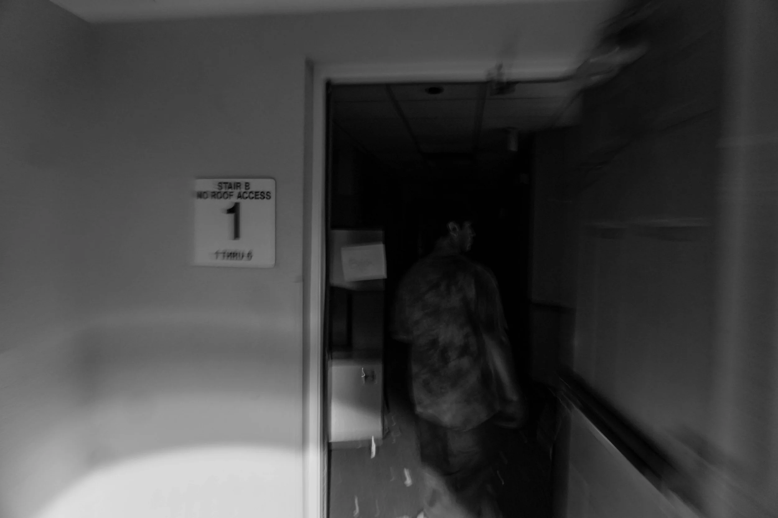 Person walking down a hospital corridor with a sign on the wall reading "Stair B No Roof Access".