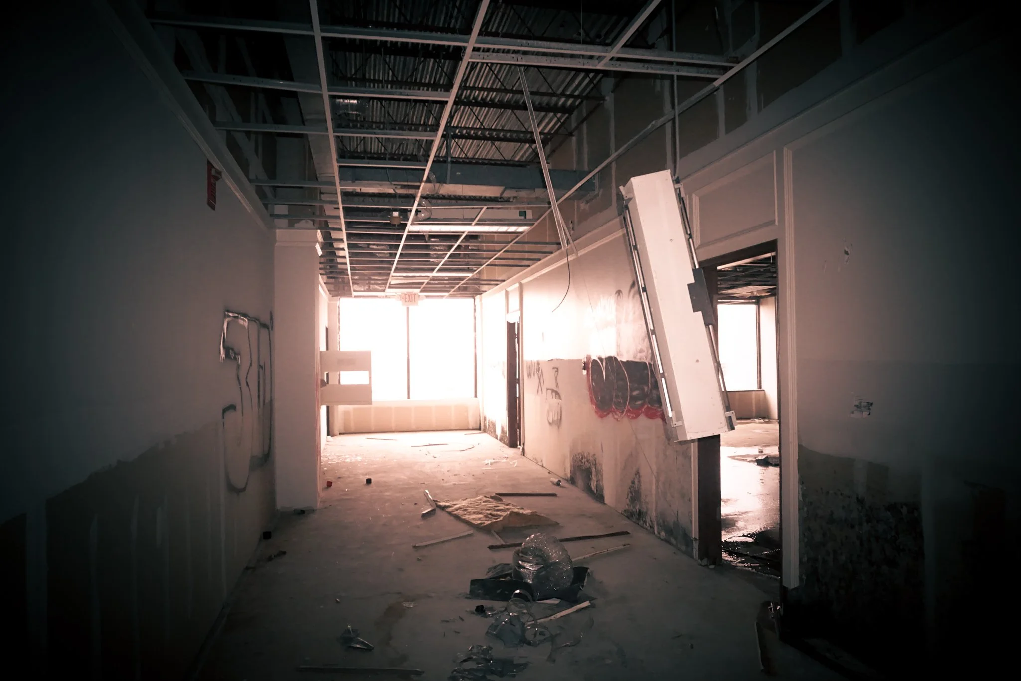 Interior of a building under construction or renovation, with exposed ceiling beams, unfinished walls, construction debris on the floor, and a leaning wall panel.
