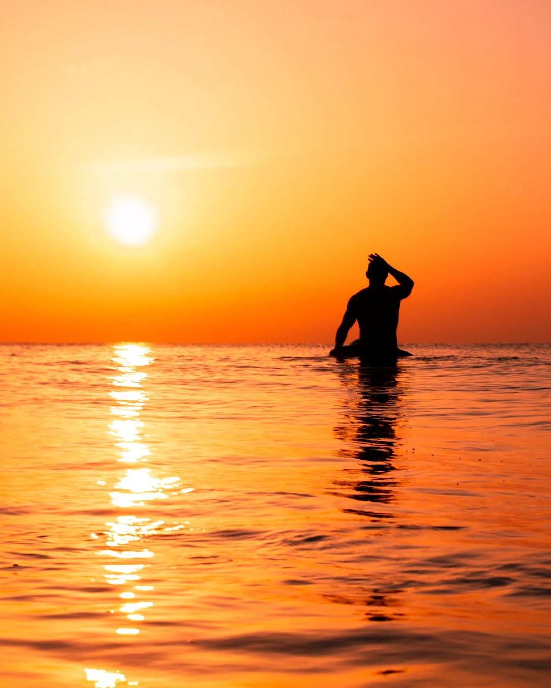 Silhouette of a person in the water during sunset, with the sun low on the horizon and reflecting on the ocean.