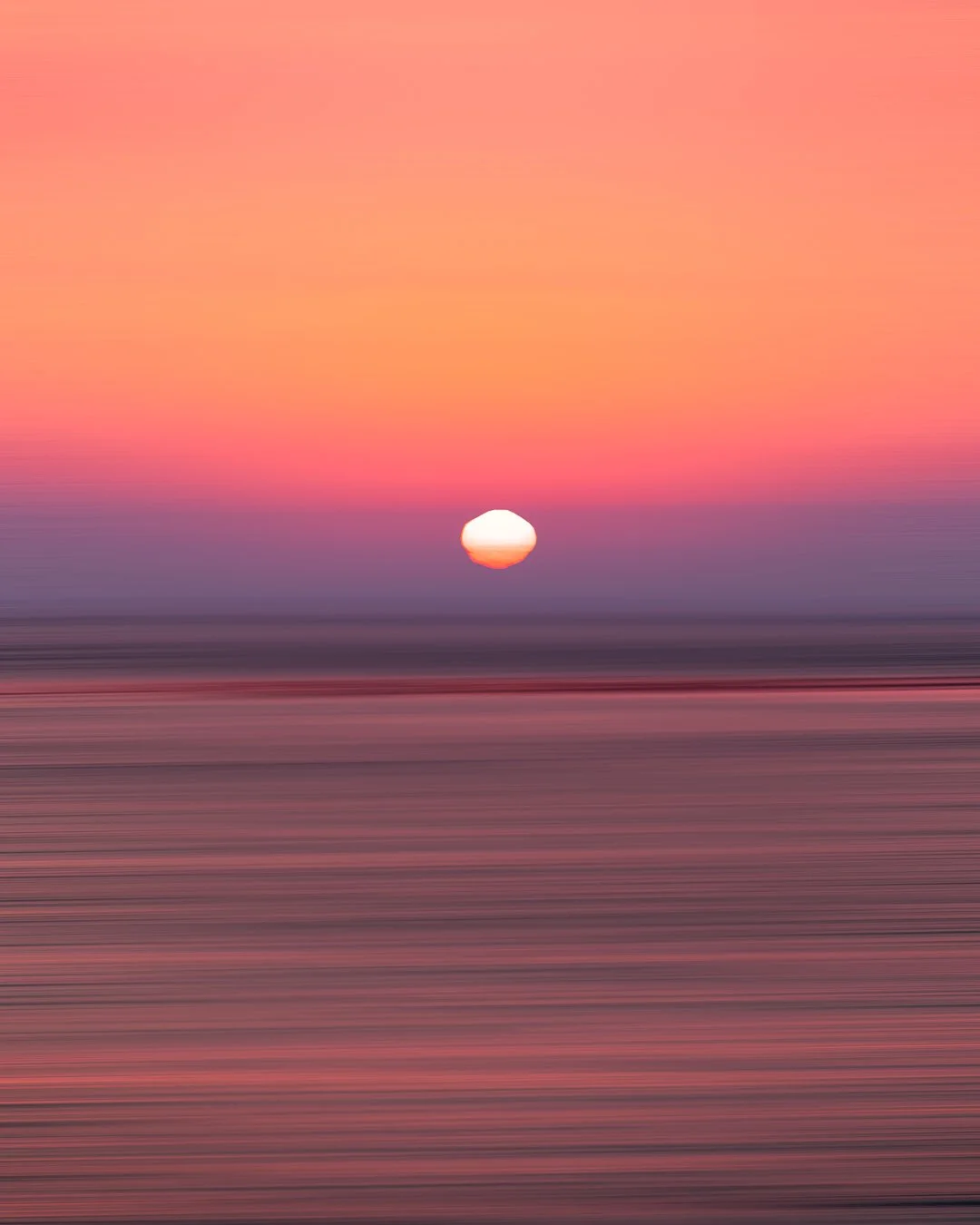 Abstract image of a sunset over the ocean with a pink and purple sky and blurred horizontal lines at the water's surface.
