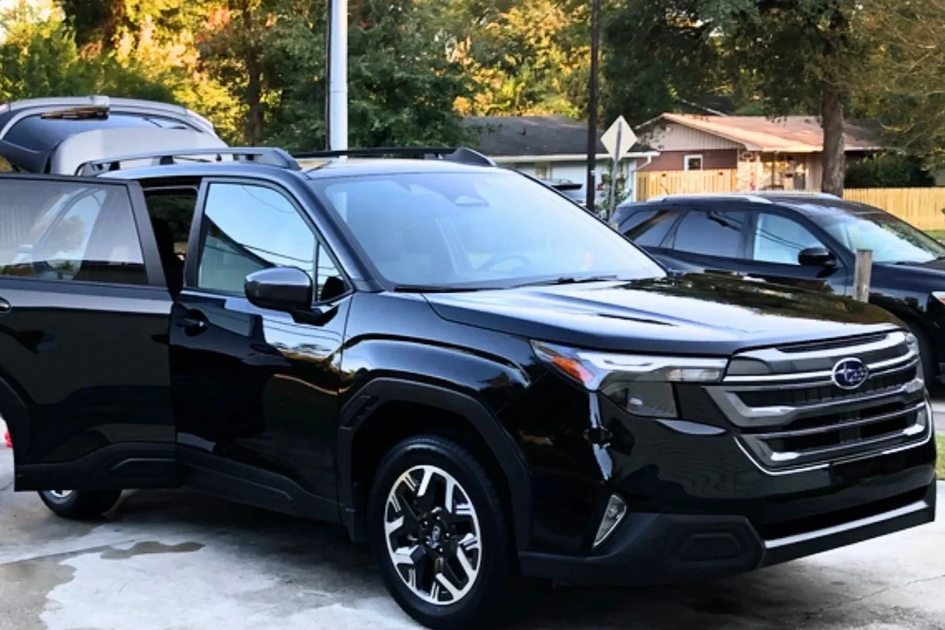 Black Subaru SUV parked in a driveway with houses and trees in the background.
