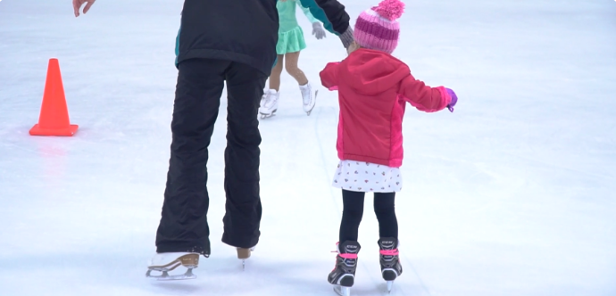 A young beginner learning to ice skate with an instructor at Aliso Viejo Ice Palace