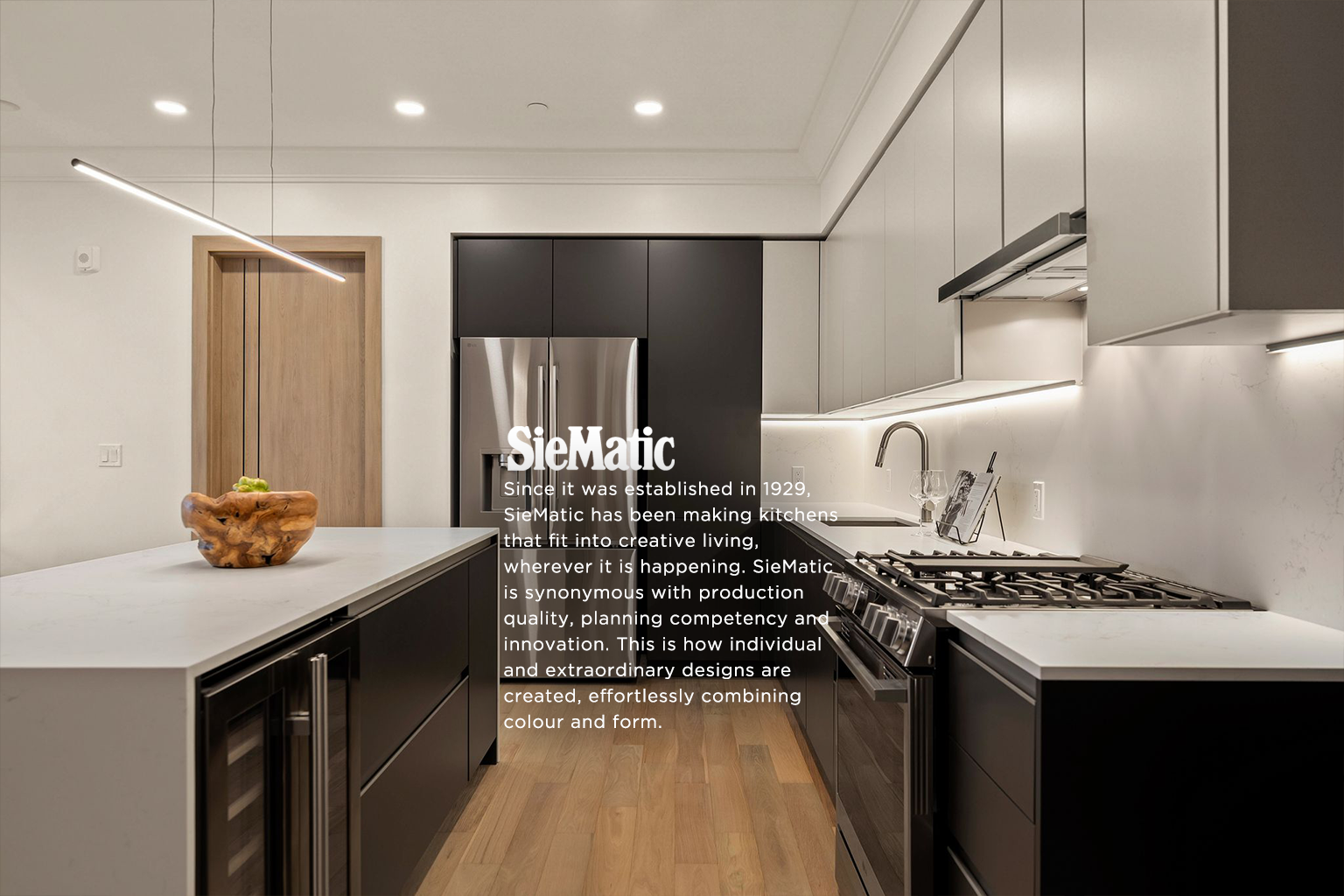 Modern kitchen with gray and black cabinets, a white countertop, stainless steel refrigerator, and a wooden bowl on the island, with under-cabinet lighting.