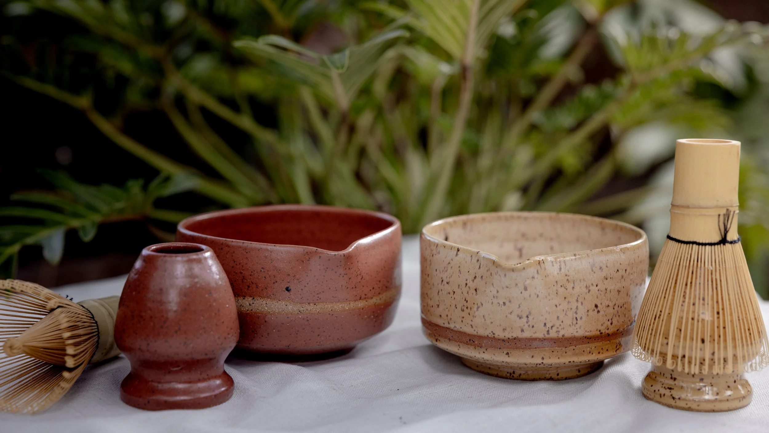 Decorative pottery and bamboo items on a white cloth with green plants in the background.