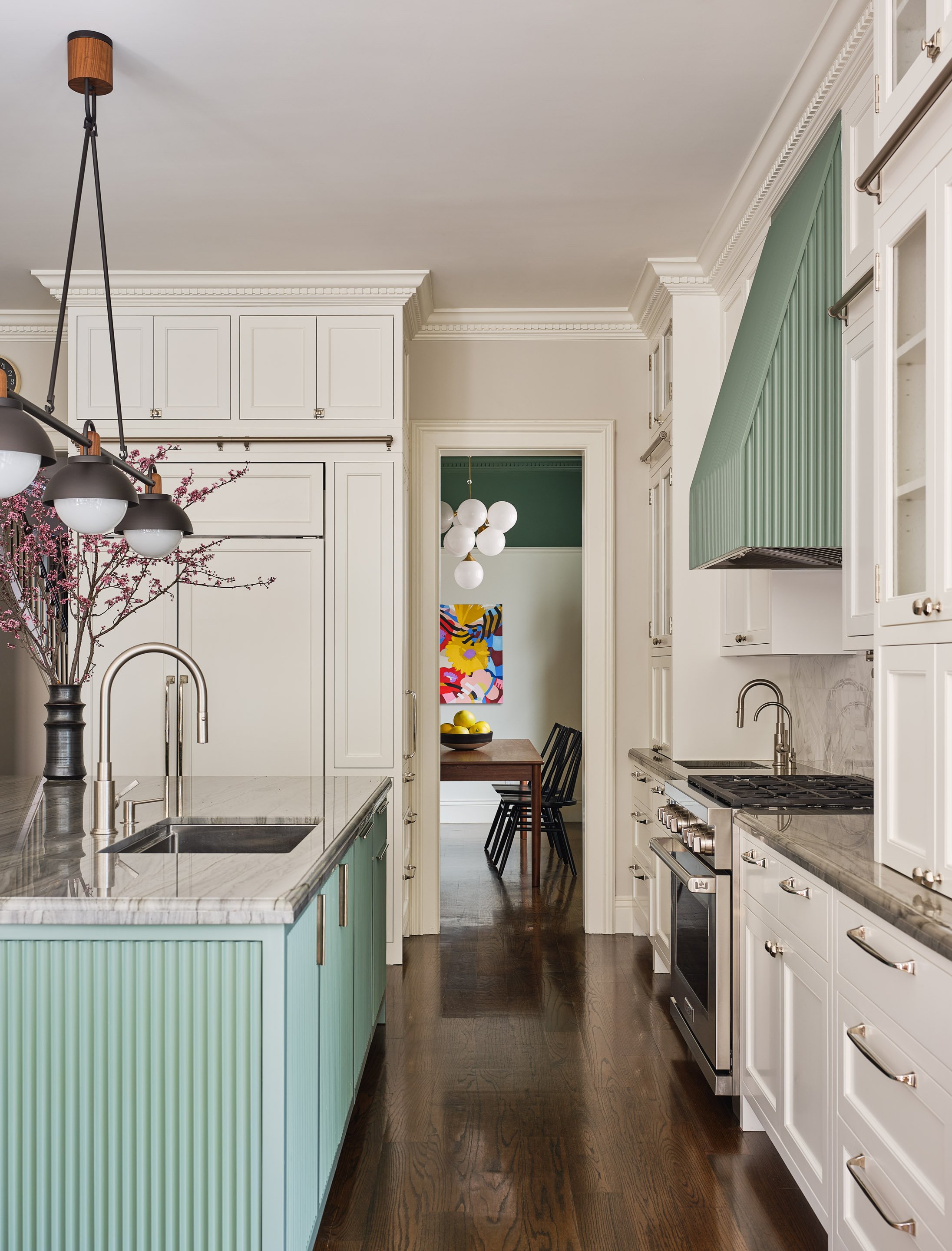 ACD | Alicia Cheung Design designed this galley kitchen with a fluted sage green range hood, a soft seafoam island, and a glimpse into a moody green dining room beyond, creating a layered and colorful space perfect for everyday cooking.