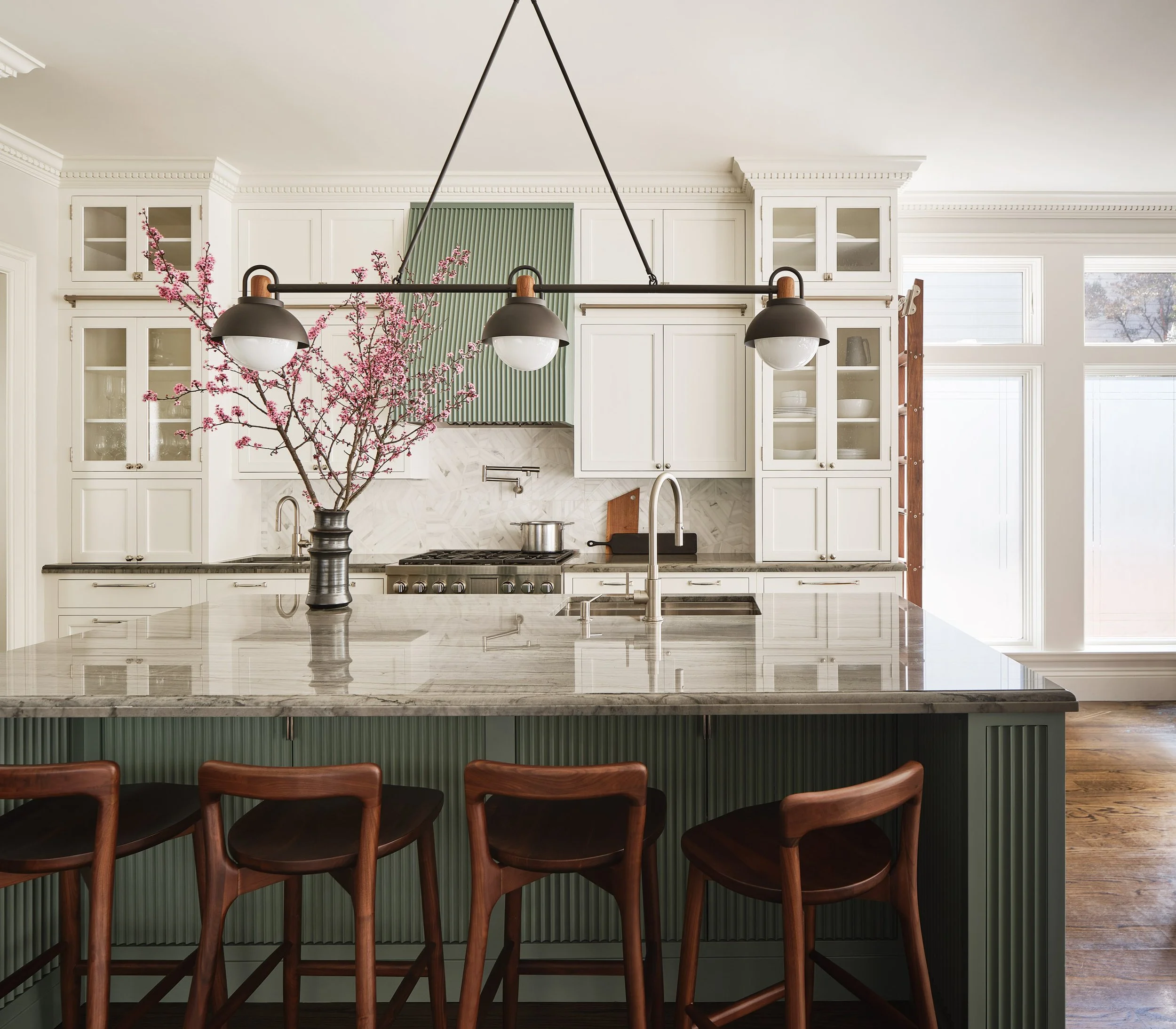 ACD | Alicia Cheung Design reimagined this kitchen with a fluted sage green island, warm white oak cabinetry, and veined marble counters, creating a sophisticated and inviting space perfect for cooking and gathering.