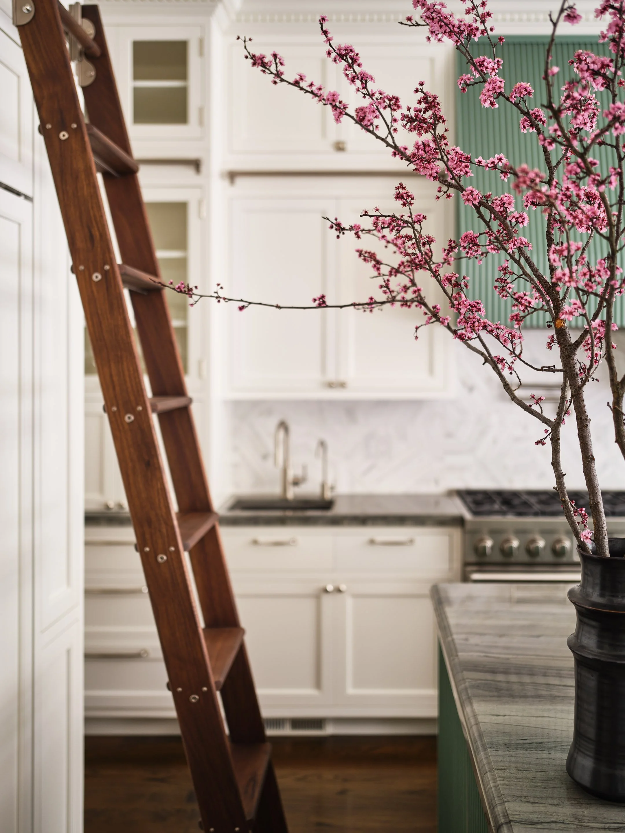 ACD | Alicia Cheung Design detailed this kitchen with a rolling library ladder, flowering cherry branches, and marble countertops, creating a warm and characterful moment perfect for everyday living.