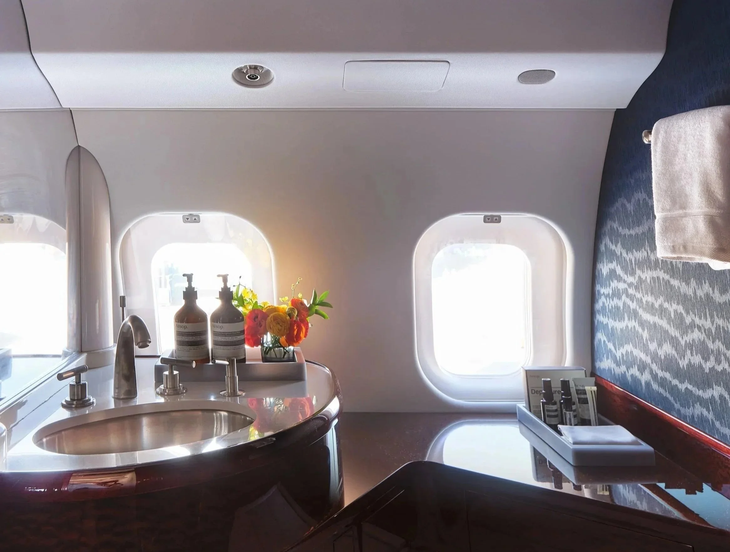 ACD | Alicia Cheung Design detailed this jet lavatory with polished nickel fixtures, wallpaper, and fresh florals, creating a refined and hotel-like moment perfect for freshening up in flight.