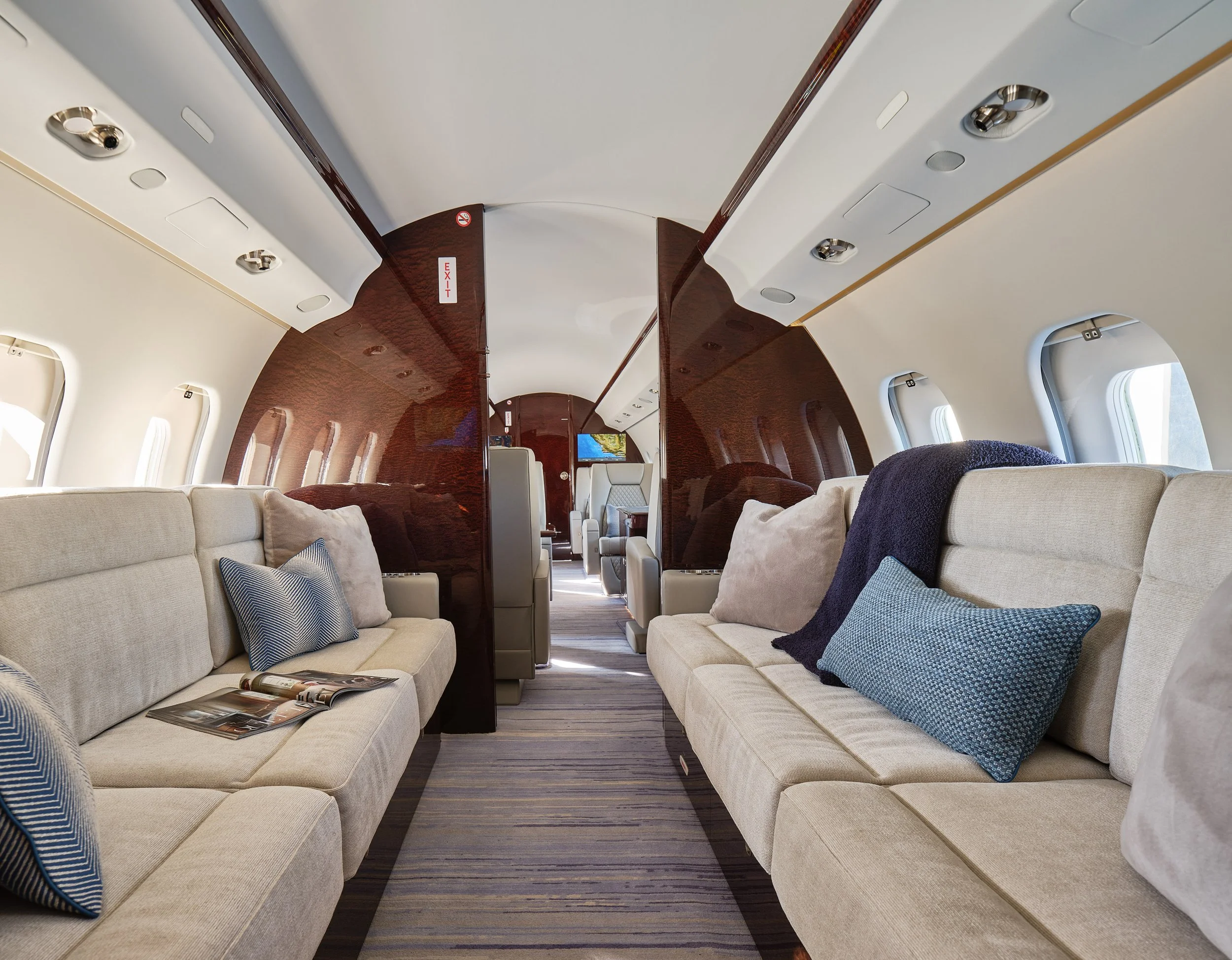 ACD | Alicia Cheung Design designed this jet lounge with plush upholstered sofas, layered blue textiles, and a chenille throw, creating a relaxed and residential space perfect for settling in mid-flight.