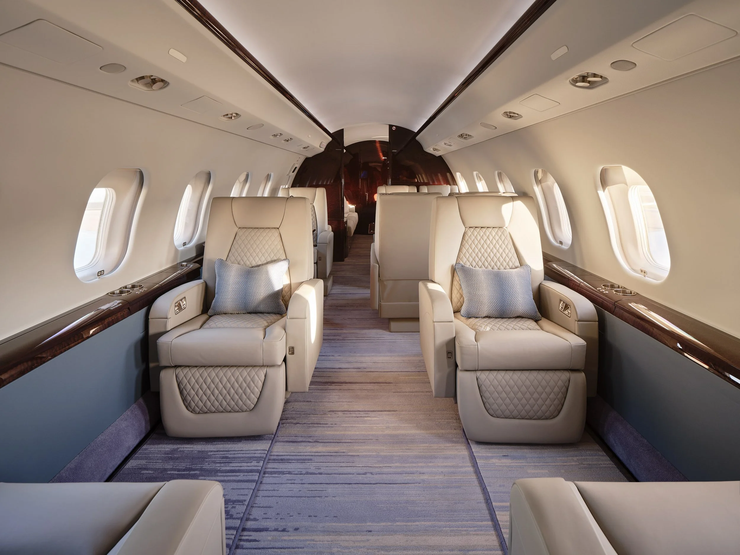ACD | Alicia Cheung Design detailed this jet cabin with quilted leather seating, custom herringbone pillows, and a patterned blue carpet runner, creating a serene and elevated space perfect for long-haul comfort.