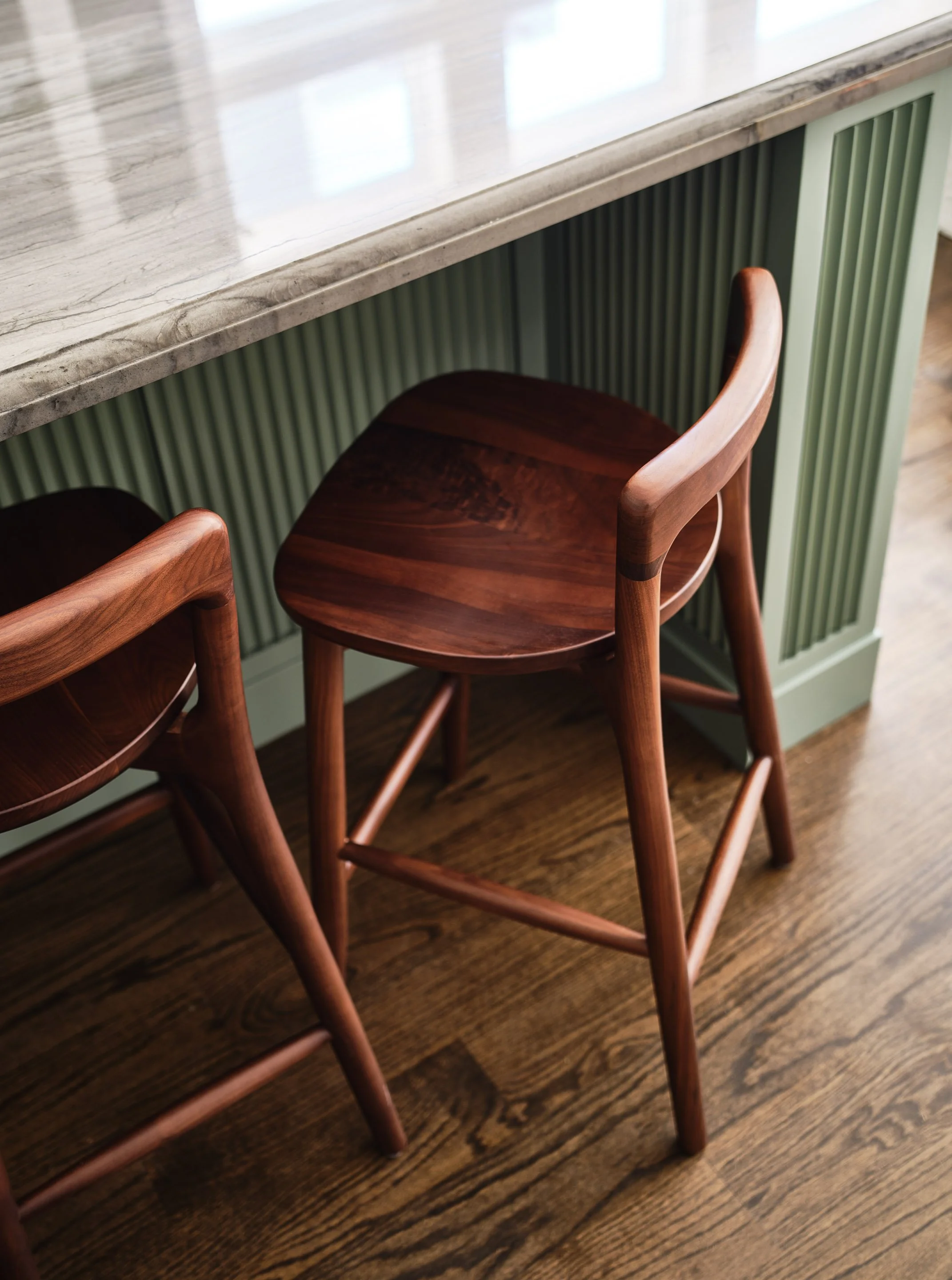 ACD | Alicia Cheung Design detailed this kitchen island with sculptural walnut counter stools, a fluted sage green base, and warm marble countertops, creating a refined and textural moment perfect for casual seating.