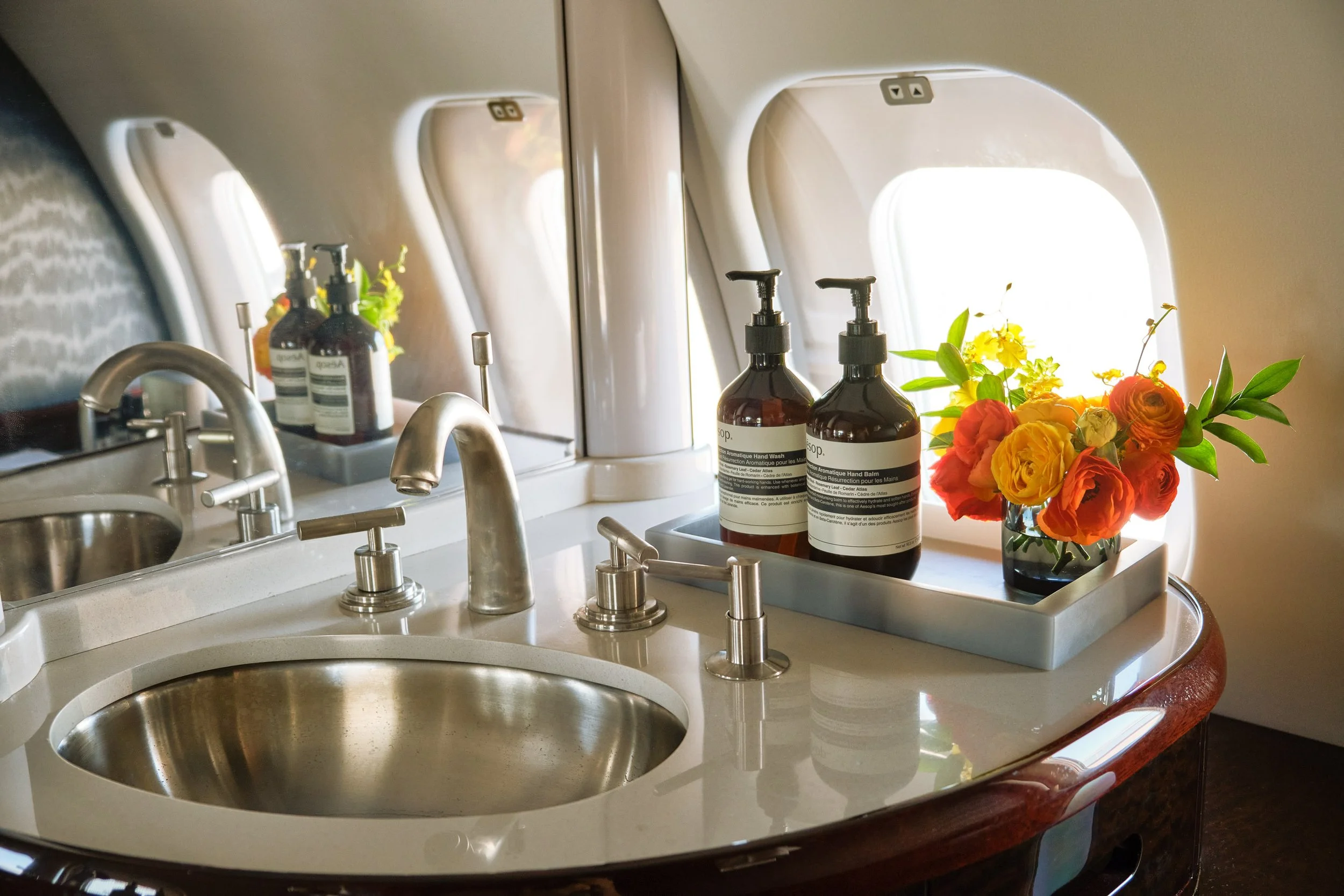 ACD | Alicia Cheung Design detailed this jet lavatory with polished nickel fixtures, wallpaper, and fresh florals, creating a refined and hotel-like moment perfect for freshening up in flight.