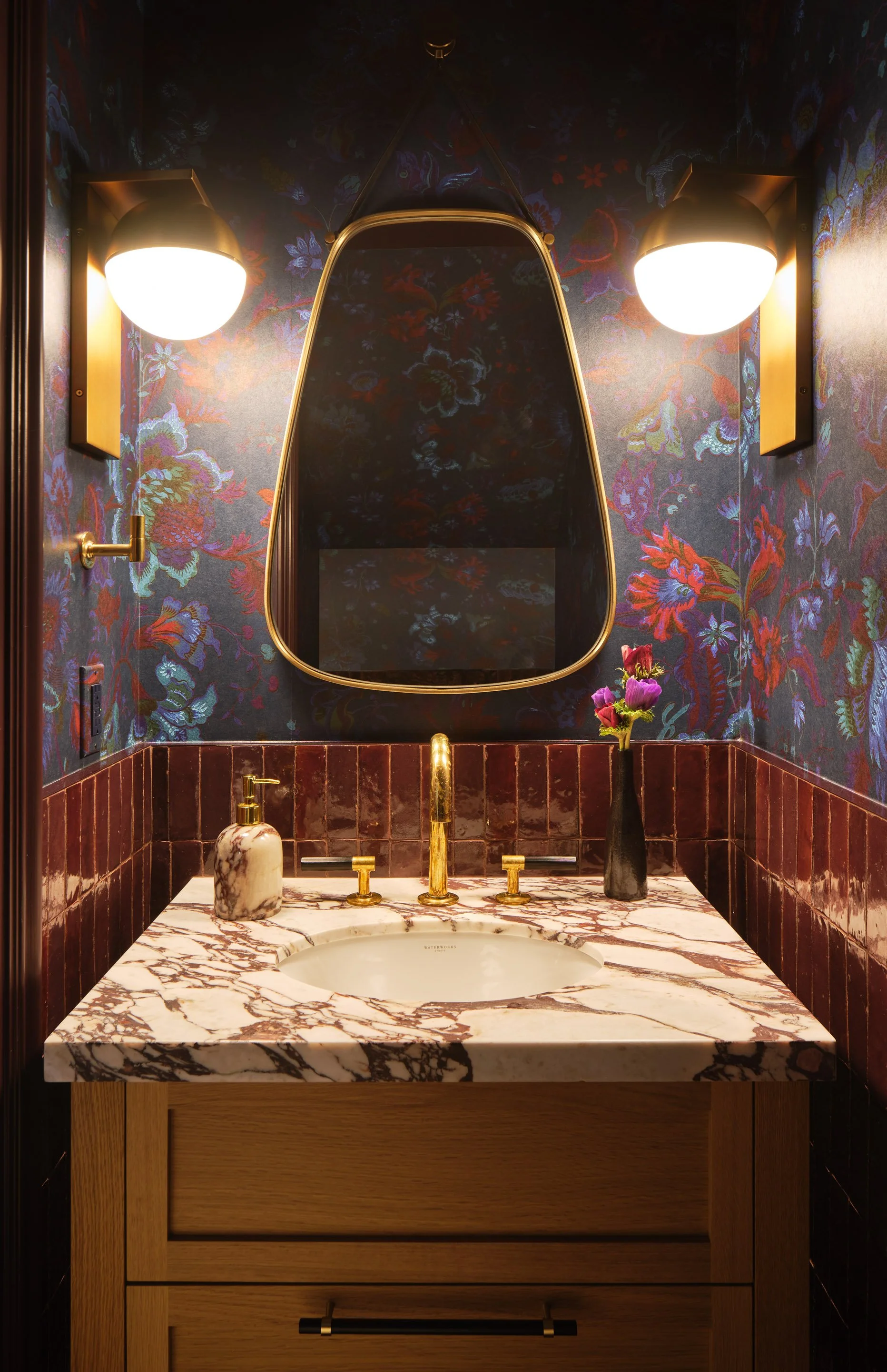 ACD | Alicia Cheung Design designed this powder room with moody floral wallpaper, brass sconces, and rich veined marble, creating a dramatic and jewel-toned space perfect for a memorable moment.
