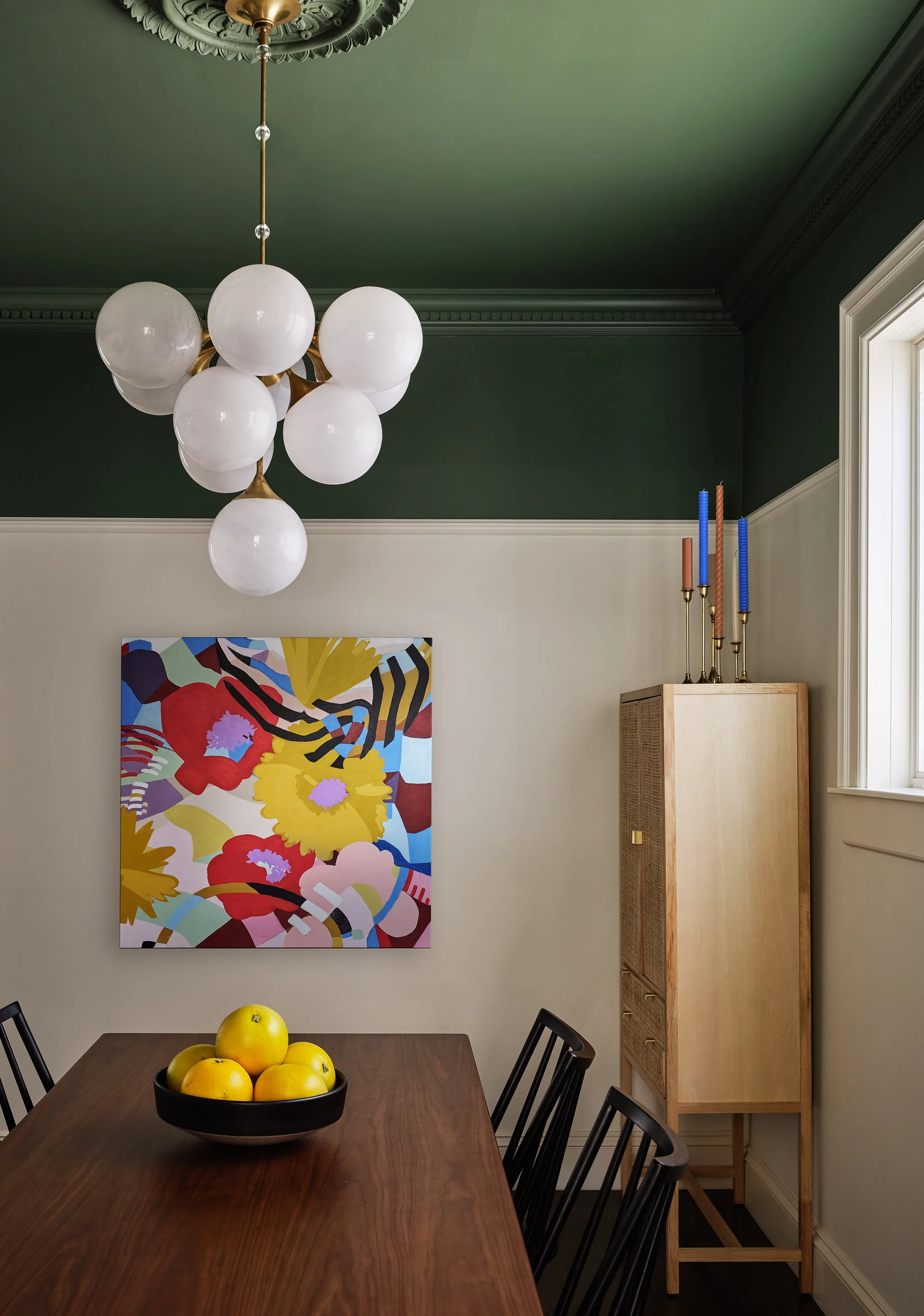 ACD | Alicia Cheung Design designed this dining room with a deep green ceiling, a sculptural glass globe chandelier, and a bold modern painting, creating a rich and playful space perfect for gathering around the table.