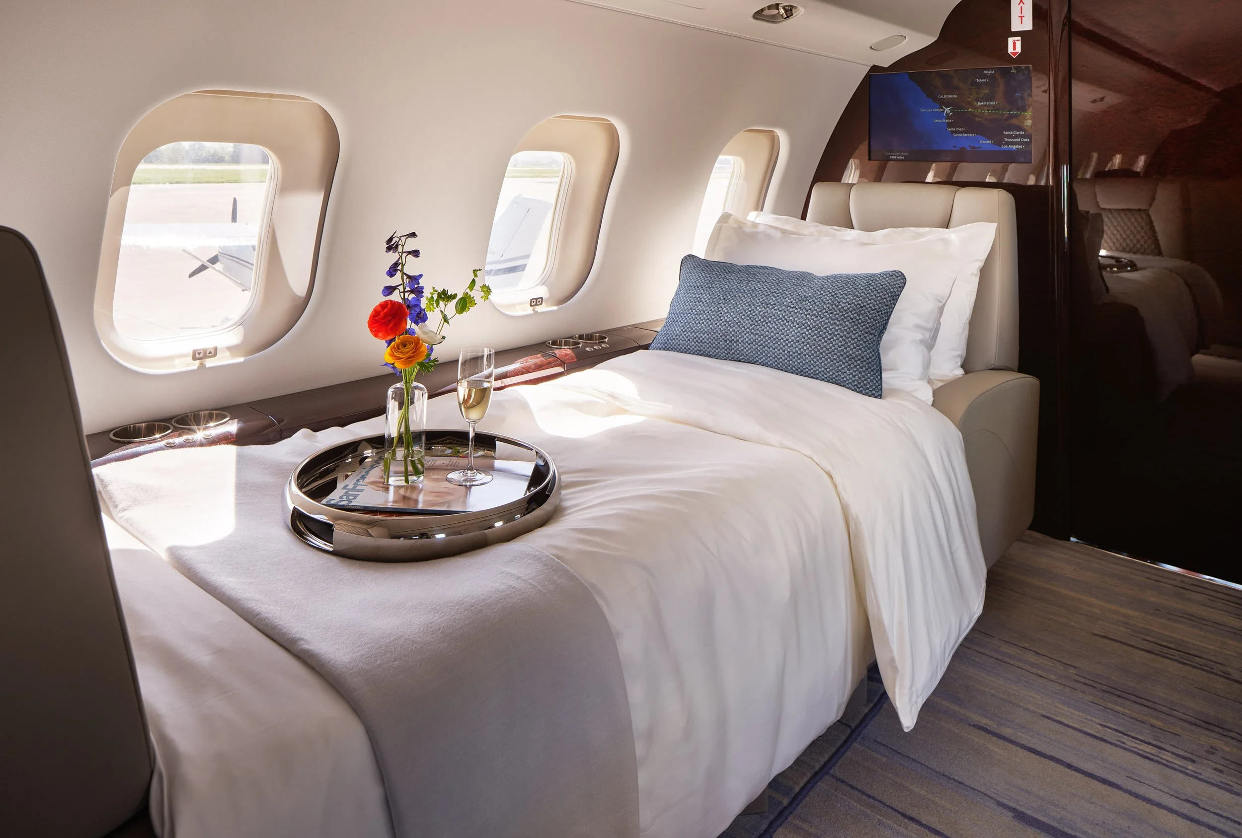 ACD | Alicia Cheung Design converted this jet seating into a full-sized bed with crisp white linens and a woven blue accent pillow, creating a restful and inviting space perfect for long-haul travel.