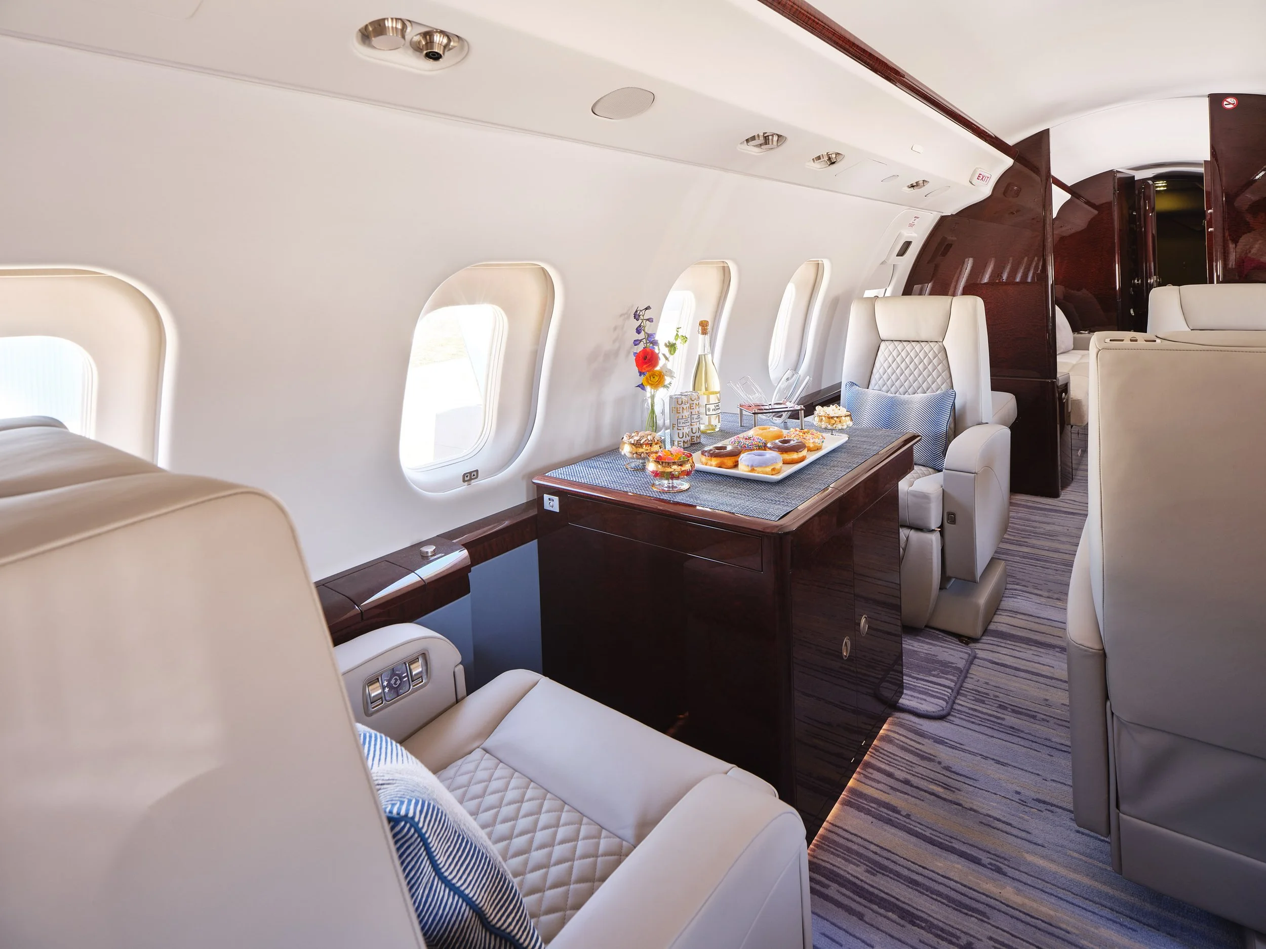 ACD | Alicia Cheung Design detailed this jet cabin with quilted leather seating, glossy burl wood tables, and a playful donut spread, creating a warm and inviting space perfect for a celebratory flight.