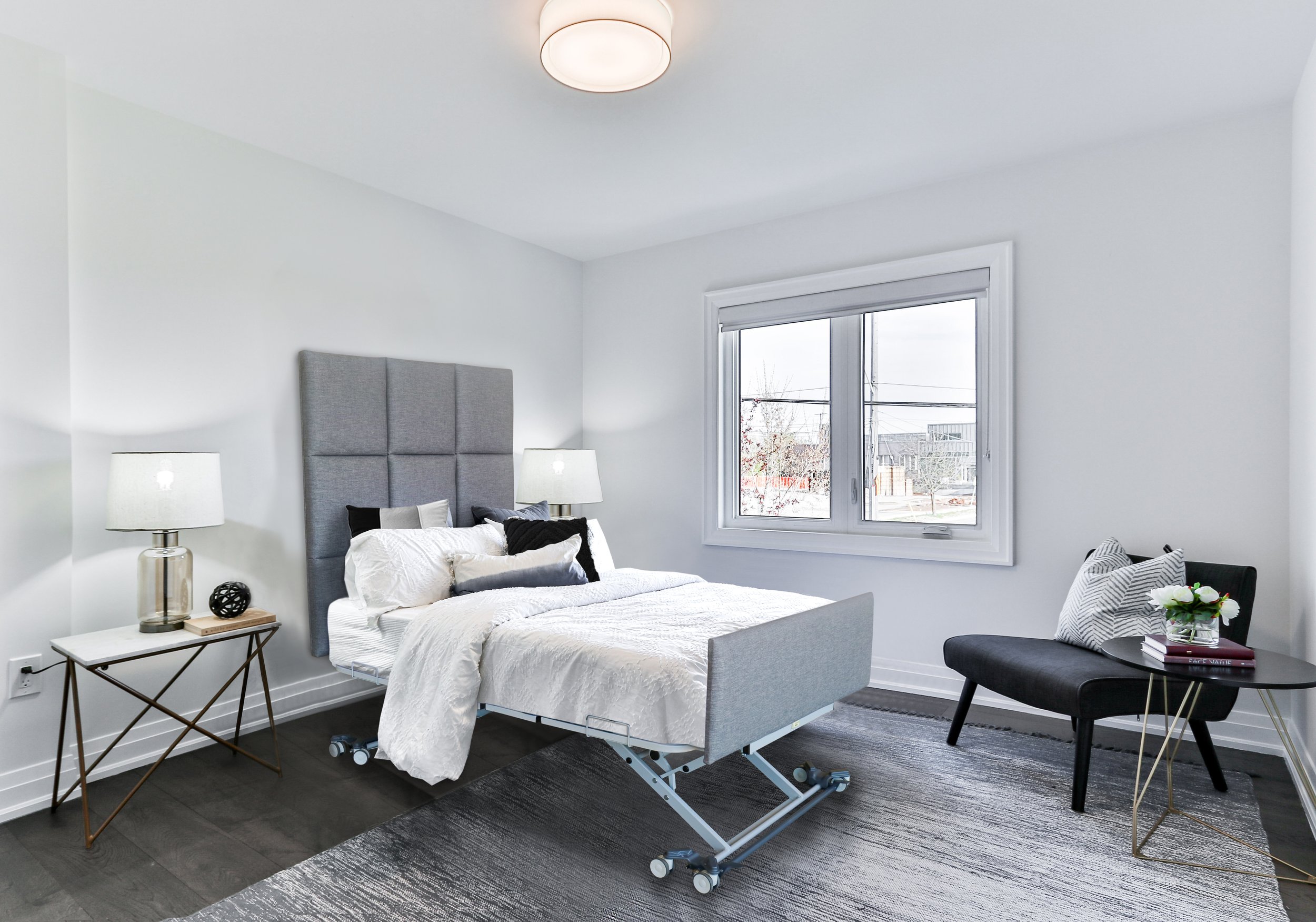 Modern bedroom with adjustable bed, gray upholstered headboard, side tables with lamps, and a window view.