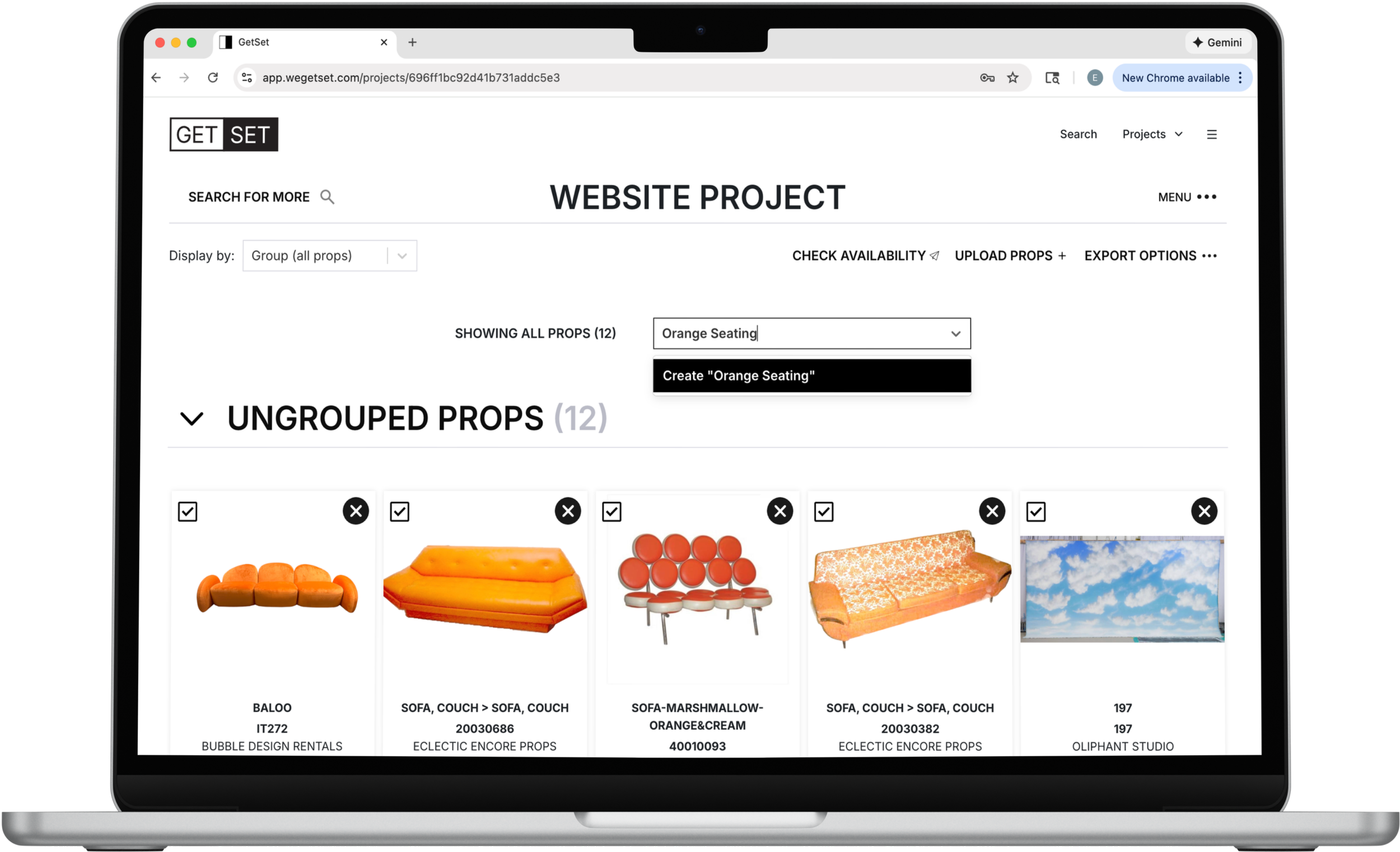 A computer screen displaying a website project interface with furniture props, including several orange sofas and a backdrop of sky with clouds.
