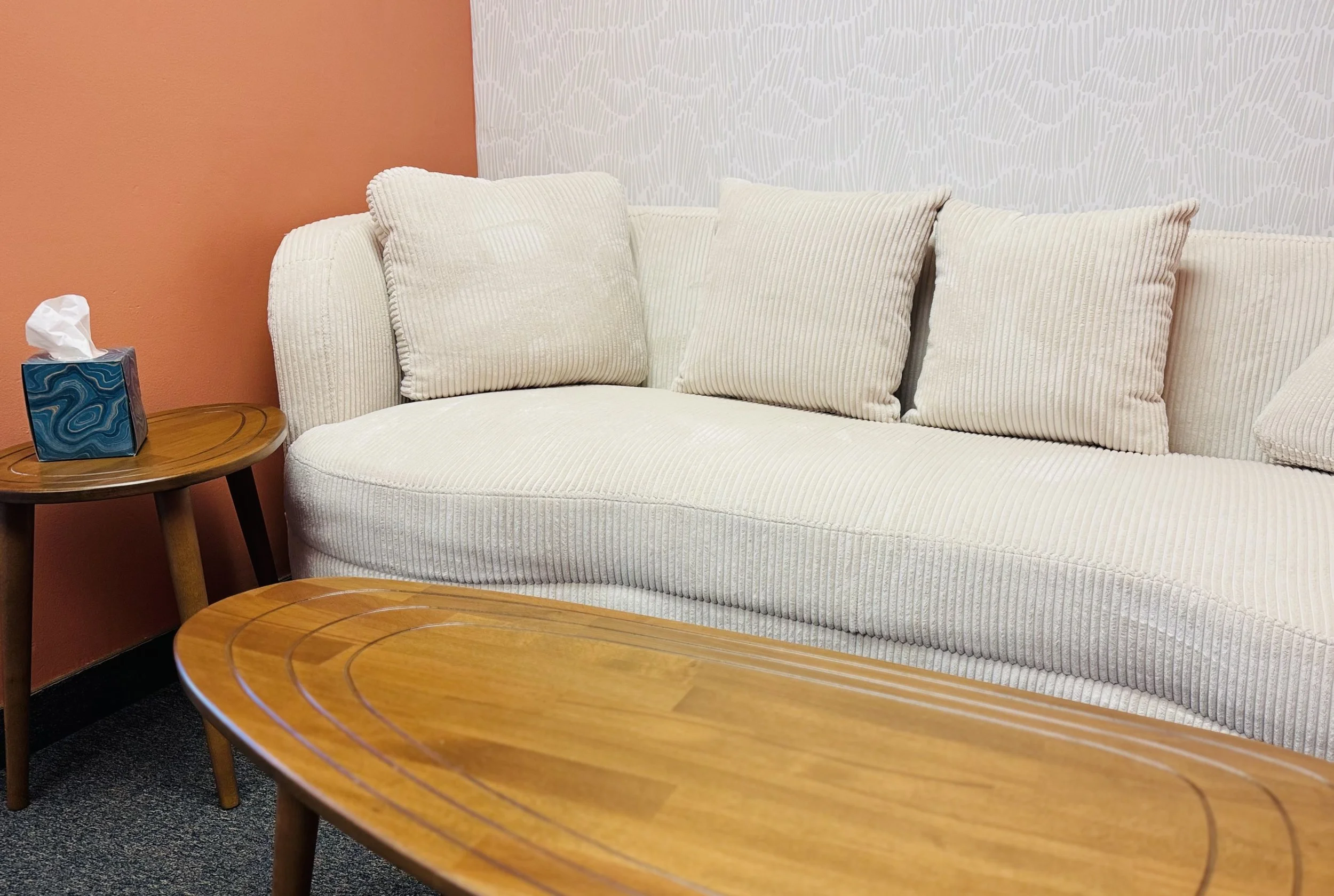 Beige color couch for clients to sit on. Oval shaped coffee and end table near it.