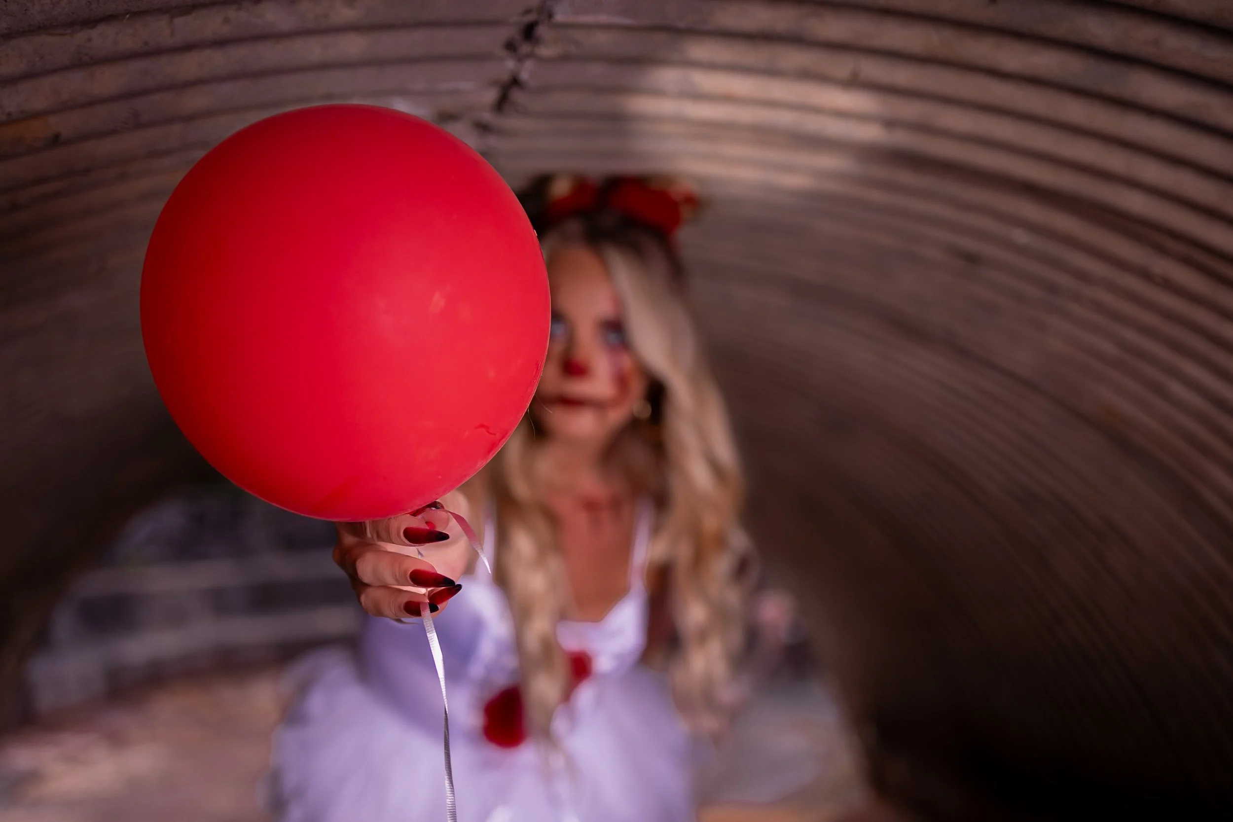 A woman dressed as a clown holding a red balloon in a tunnel