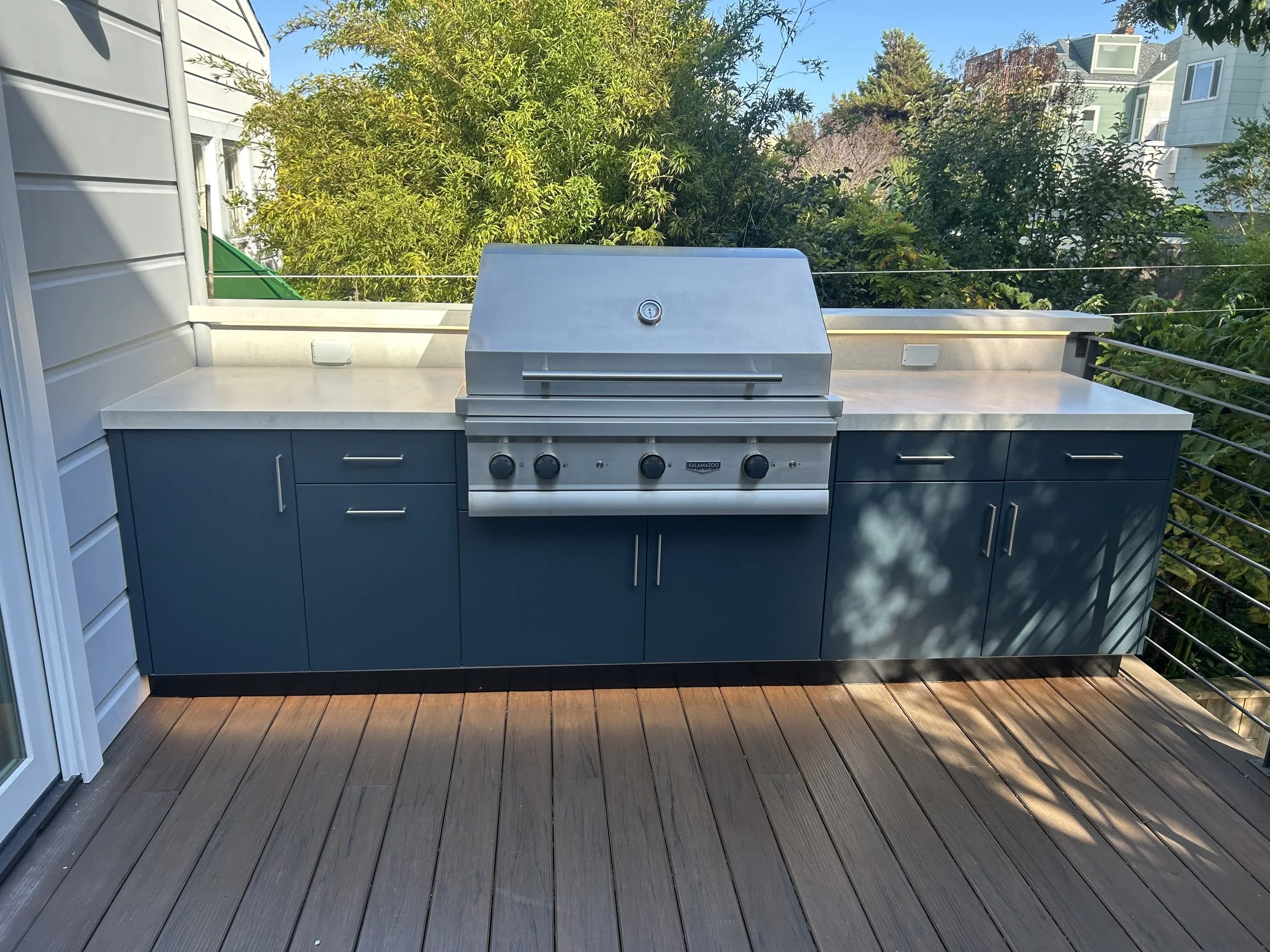 Deck-mounted outdoor kitchen with dark cabinets and a stainless steel grill.