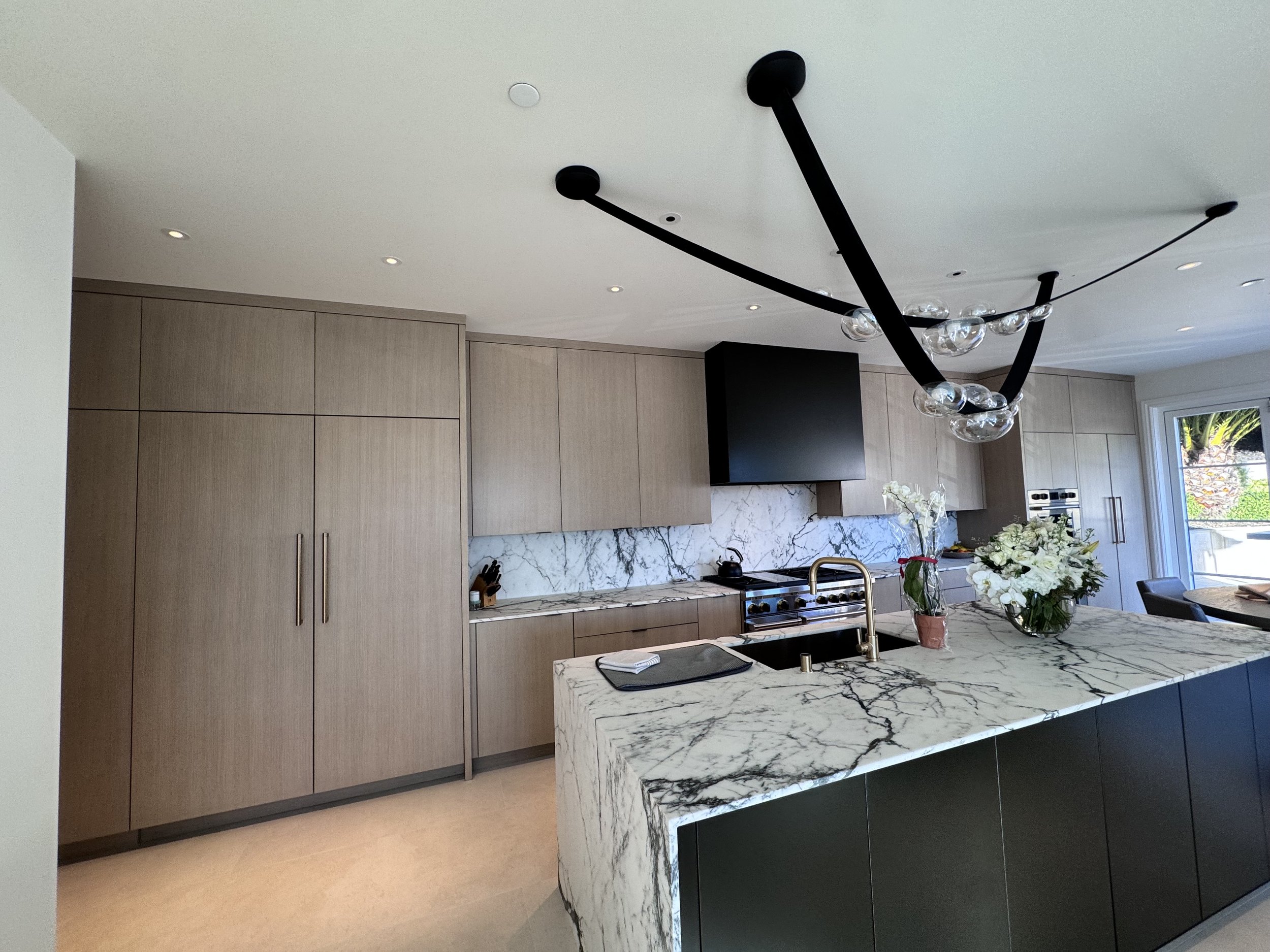 Kitchen with wood cabinets, a veined stone island, and dark pendant lighting.