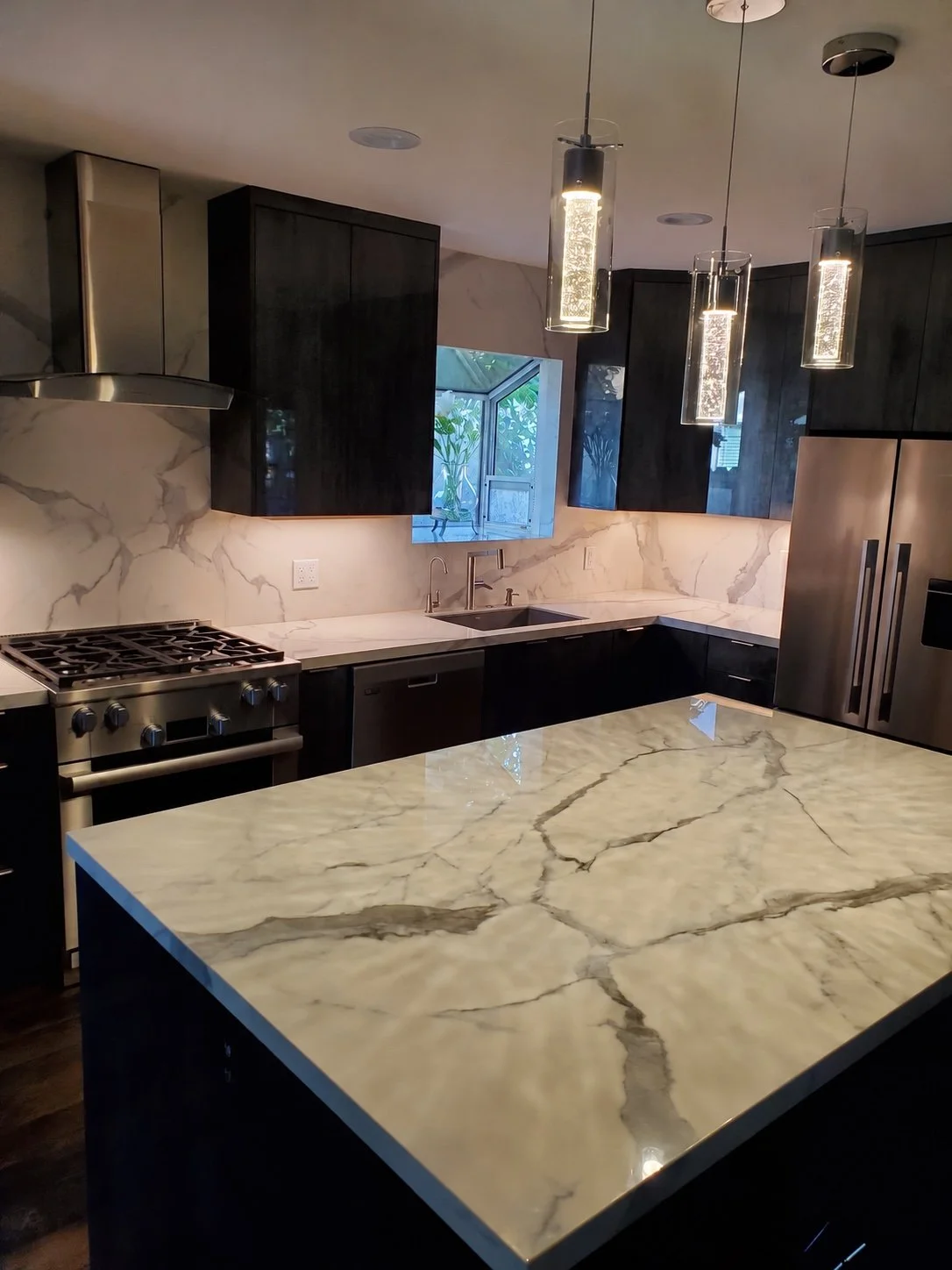 Modern kitchen with dark cabinetry, a veined stone island, matching backsplash, and integrated appliances.